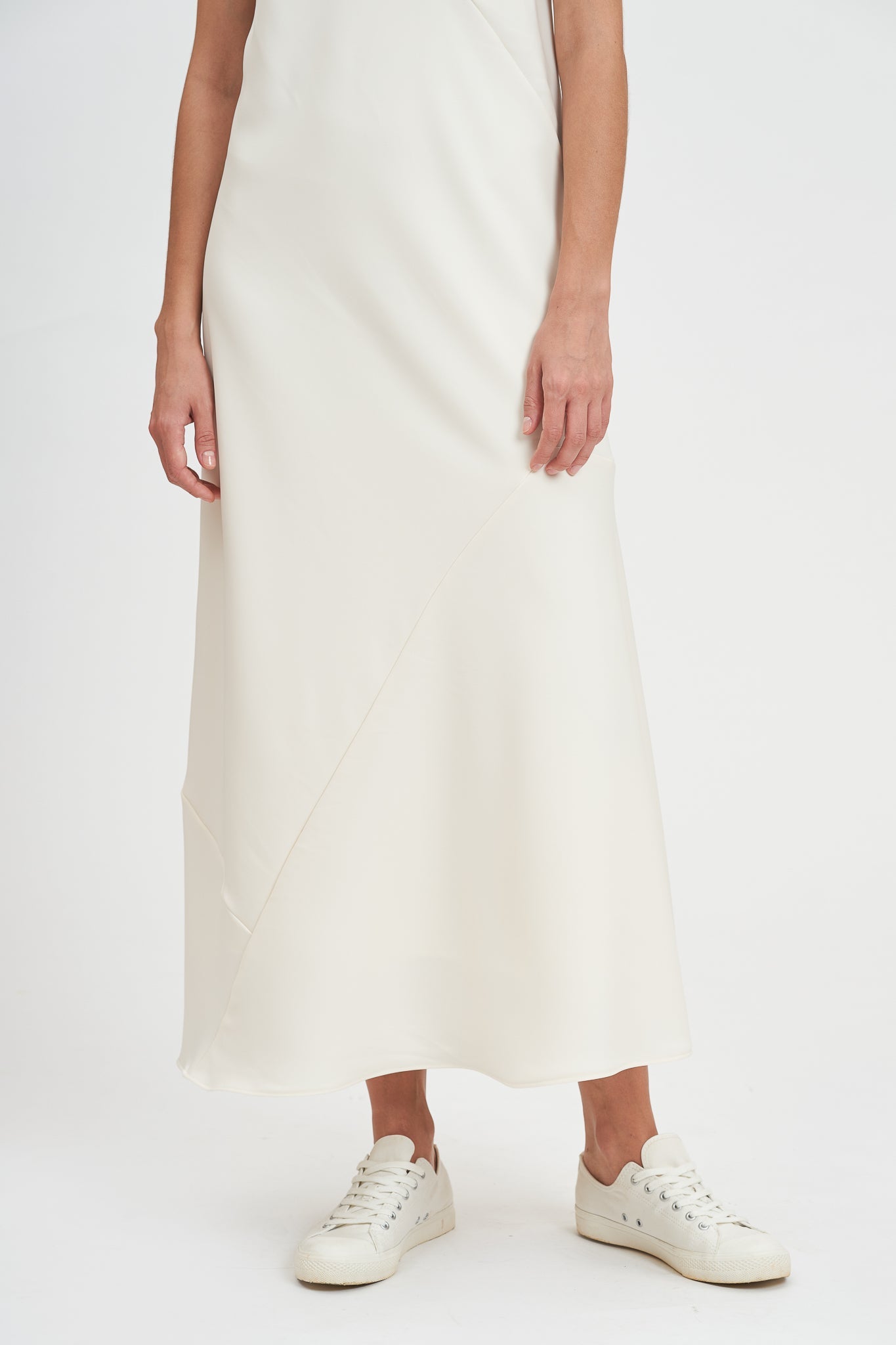 A woman with shoulder length hair is wearing an ankle length white scrappy dress. She is wearing white tennis shoes.