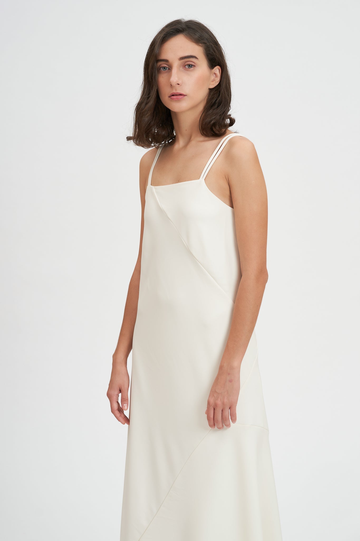 A woman with shoulder length hair is wearing an ankle length white scrappy dress.