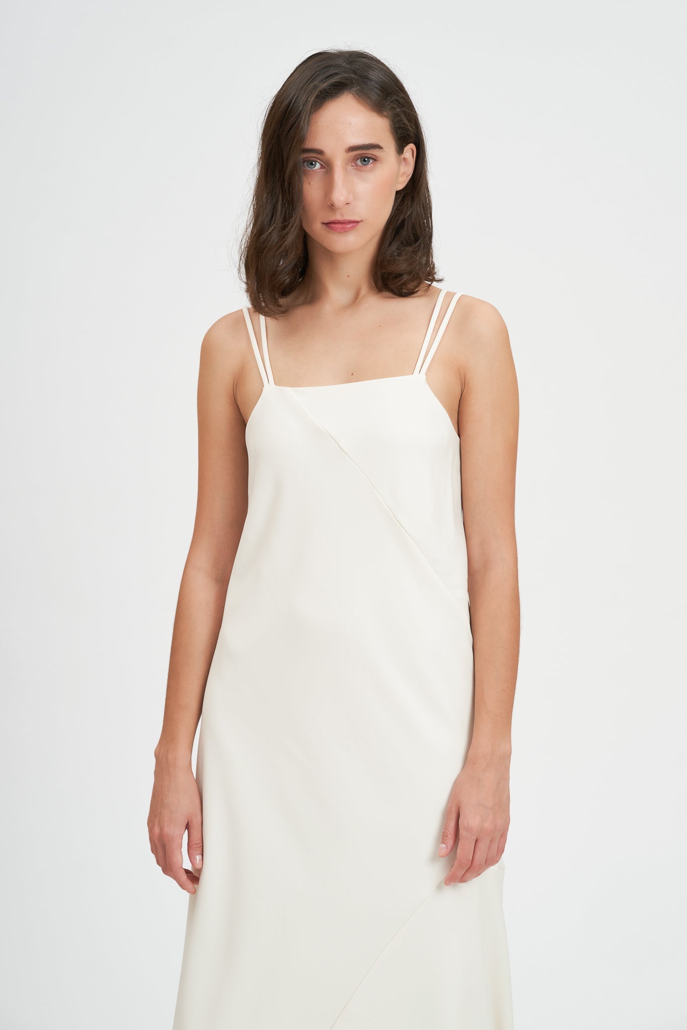 A woman with shoulder length hair is wearing an ankle length white scrappy dress.