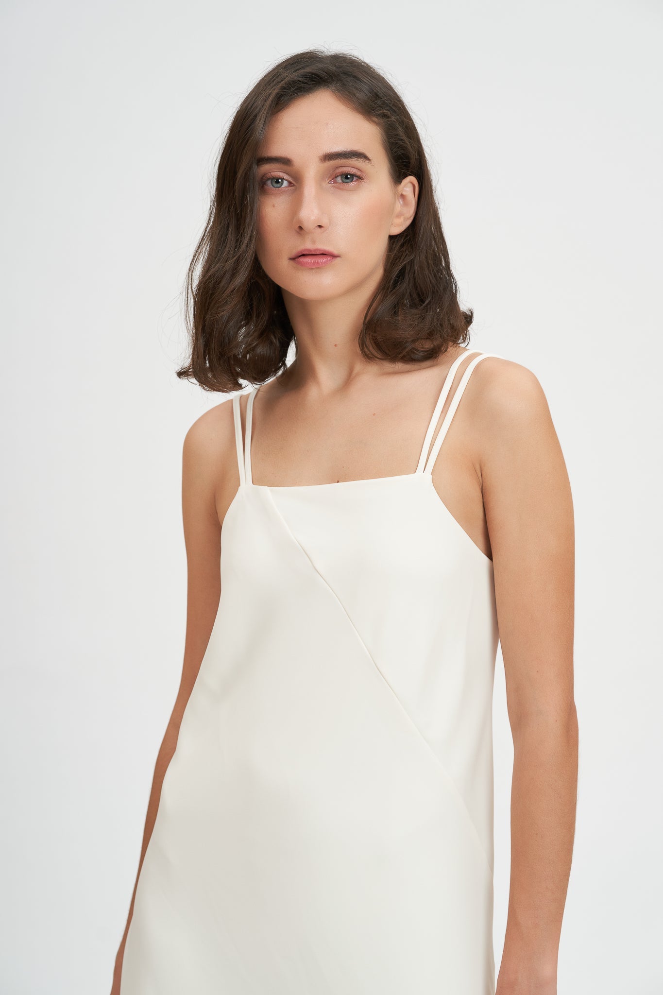 A woman with shoulder length hair is wearing an ankle length white scrappy dress.