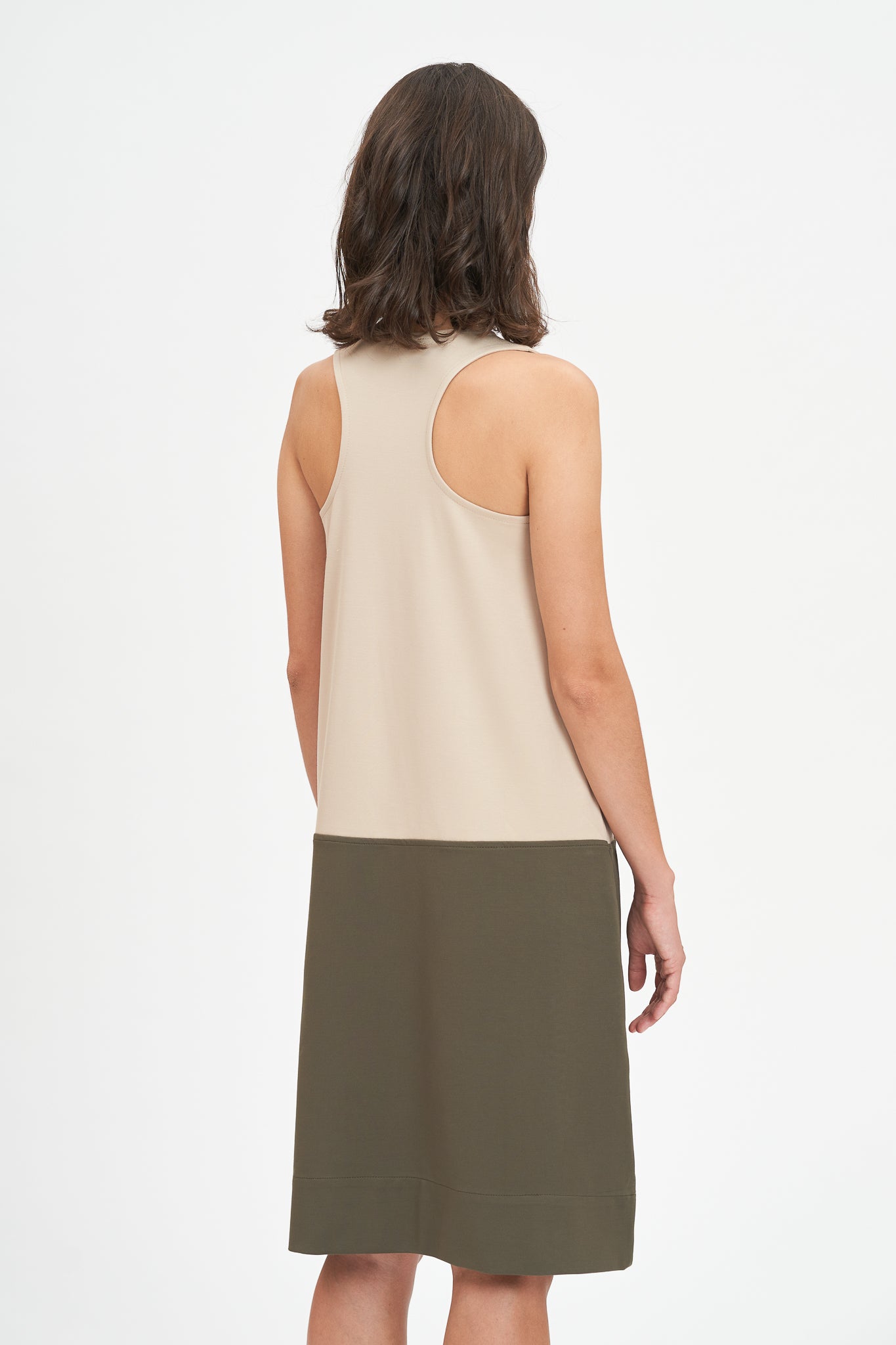 A woman with shoulder length brown hair is wearing a knee length green and nude dress.