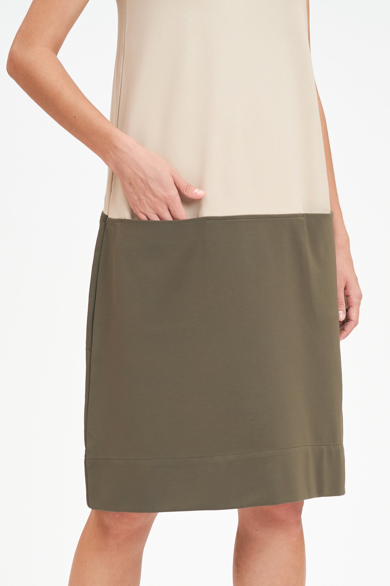 A woman with shoulder length brown hair is wearing a knee length green and nude dress.