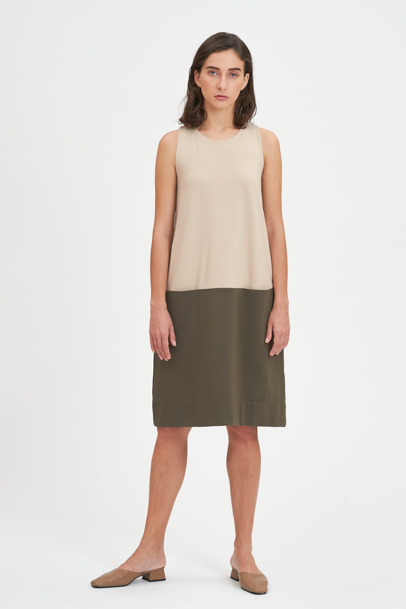 A woman with shoulder length brown hair is wearing a knee length green and nude dress. She is also wearing beige leather shoes.