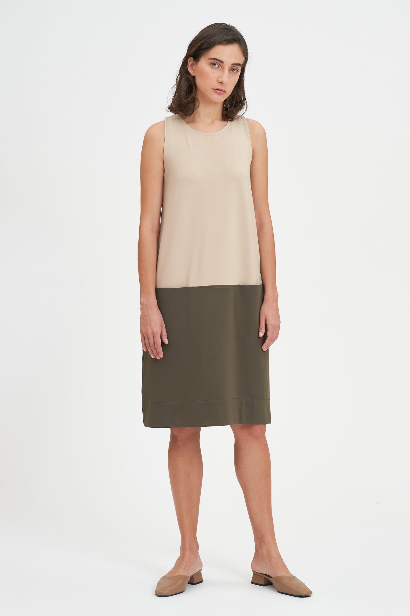 A woman with shoulder length brown hair is wearing a knee length green and nude dress. She is also wearing beige leather shoes.