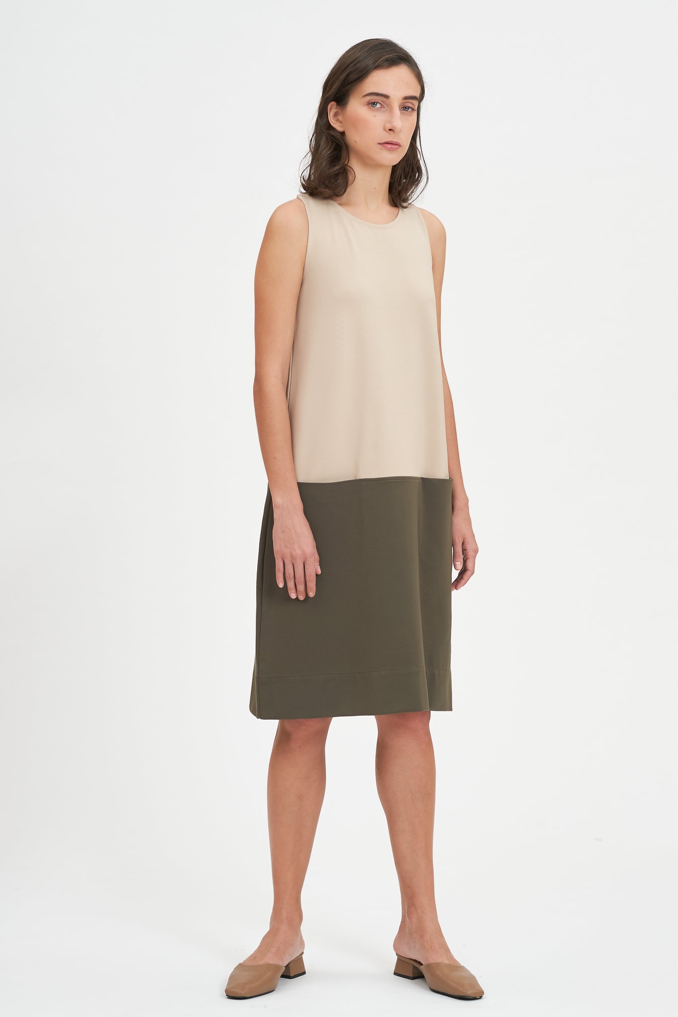 A woman with shoulder length brown hair is wearing a knee length green and nude dress. She is also wearing beige leather shoes.