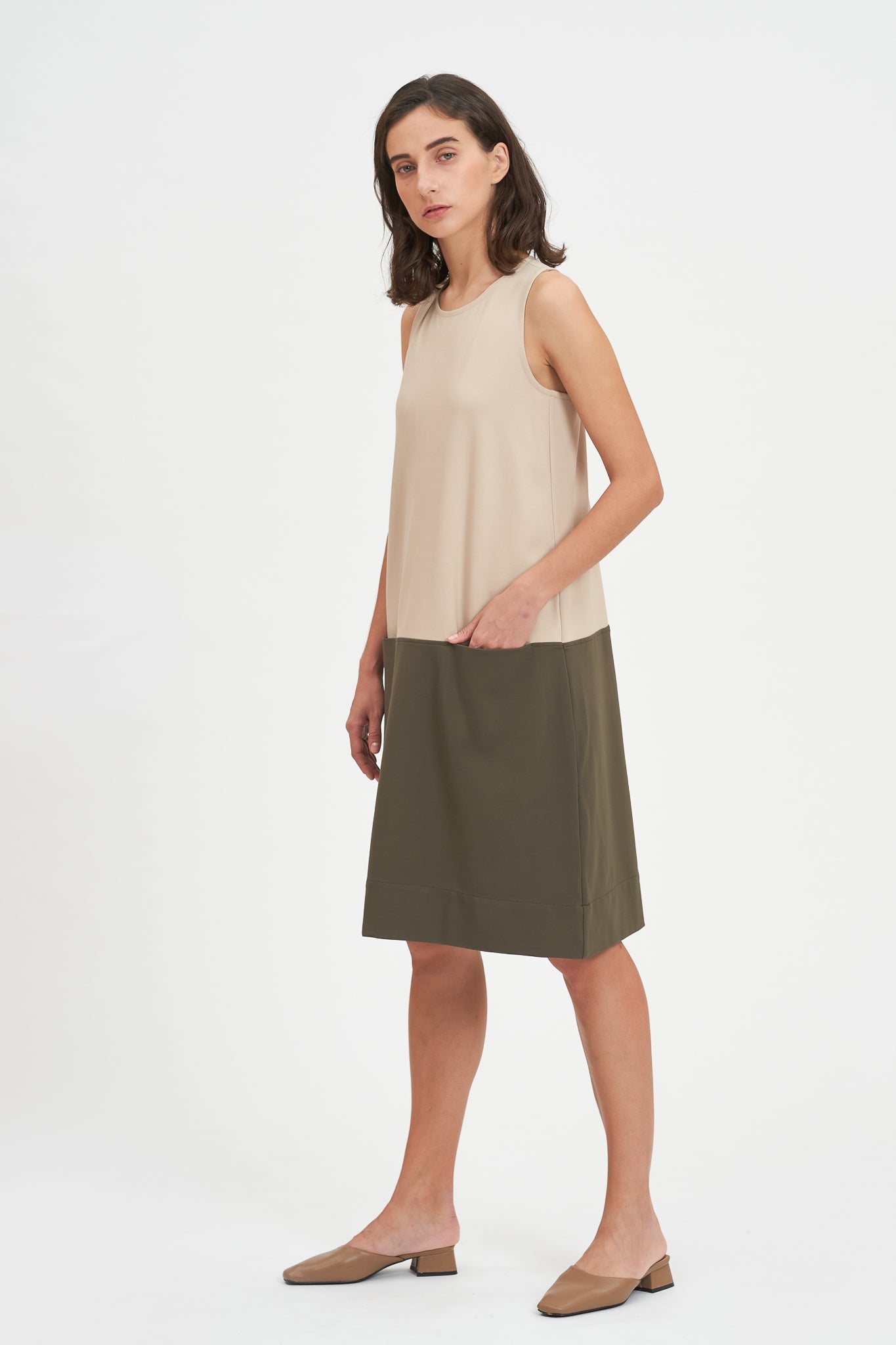 A woman with shoulder length brown hair is wearing a knee length green and nude dress. She is also wearing beige leather shoes.