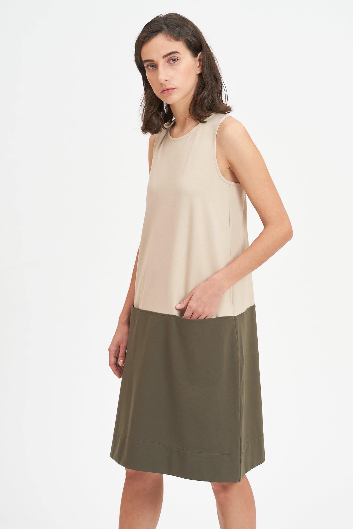 A woman with shoulder length brown hair is wearing a knee length green and nude dress.