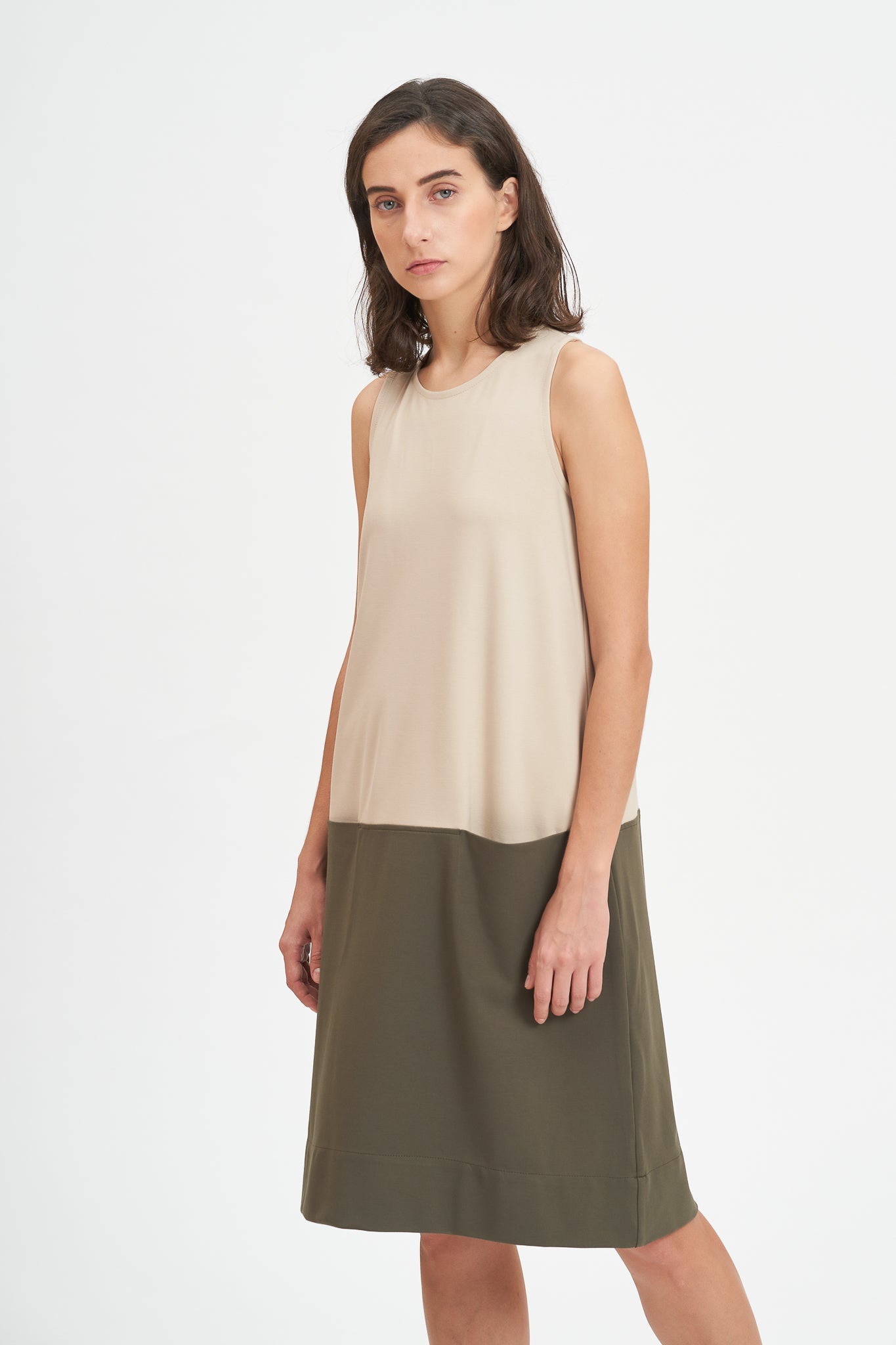 A woman with shoulder length brown hair is wearing a knee length green and nude dress.