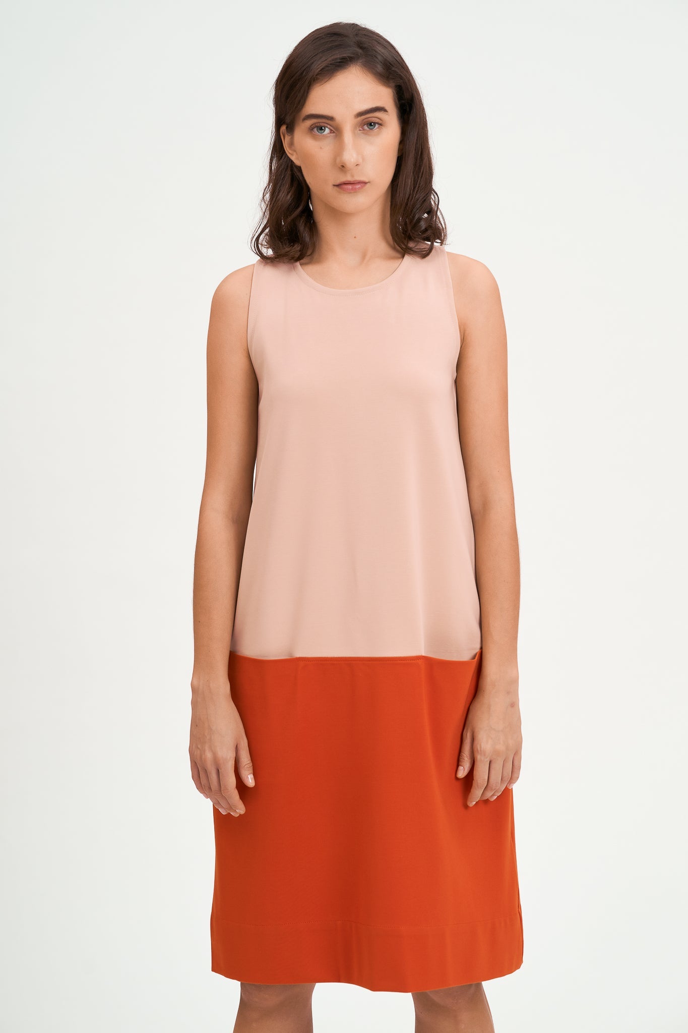 A woman with shoulder length brown hair is wearing a knee length pink and nude dress.