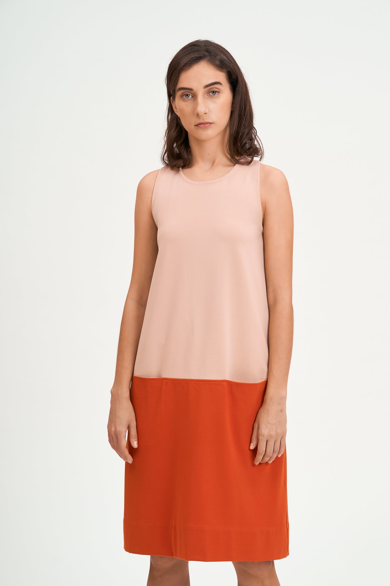 A woman with shoulder length brown hair is wearing a knee length pink and nude dress.