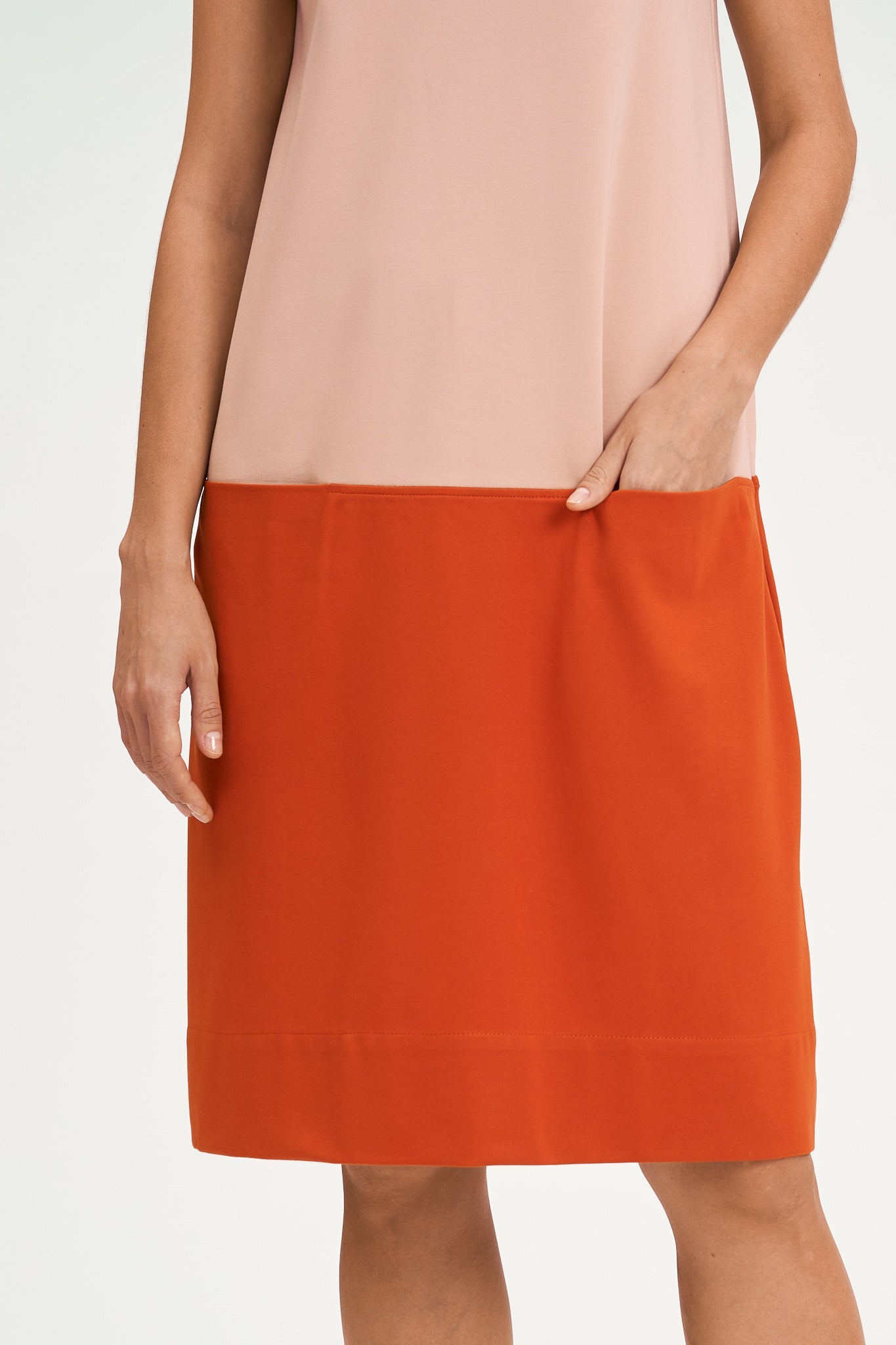 A woman with shoulder length brown hair is wearing a knee length pink and nude dress.