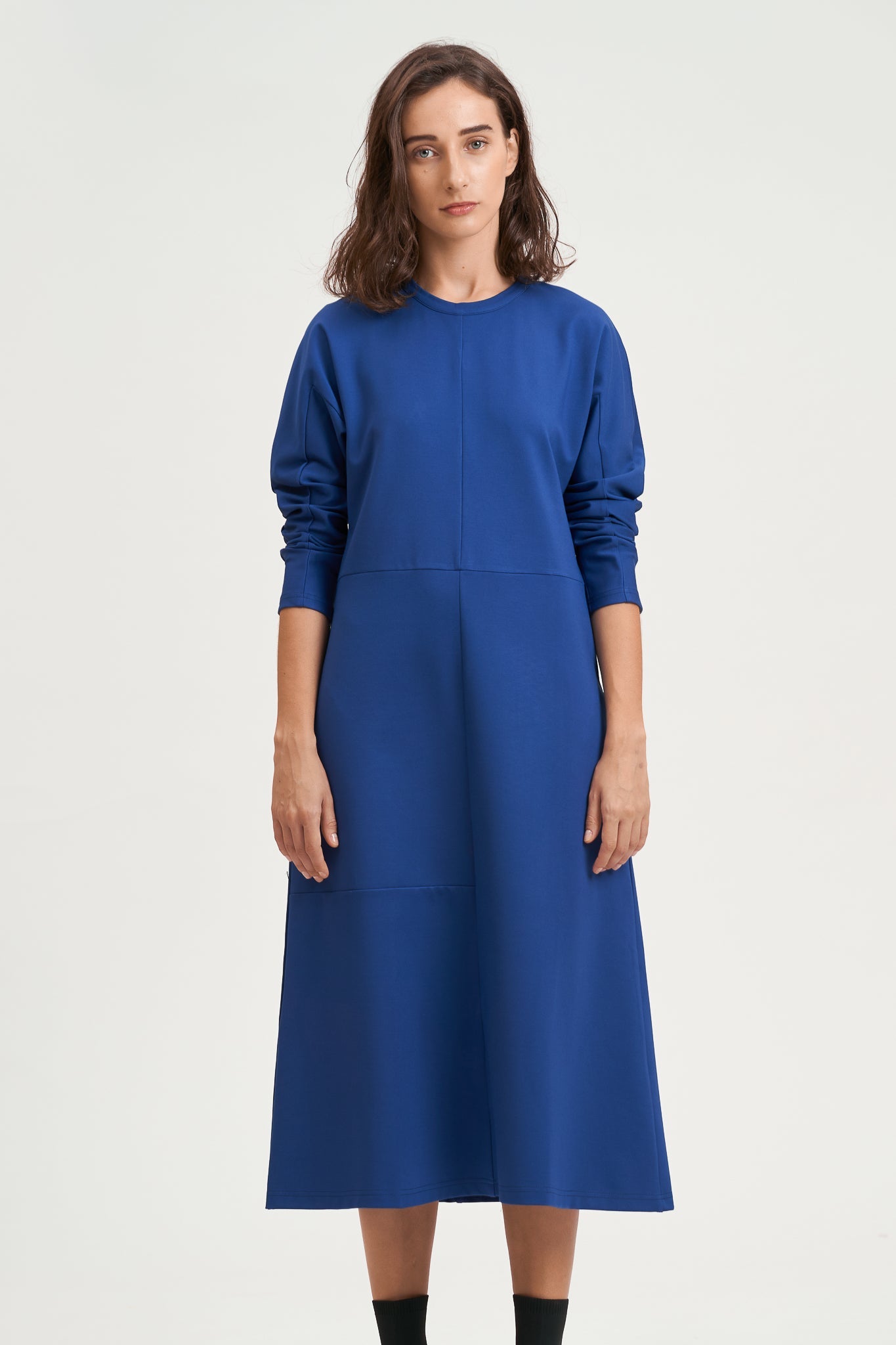 A woman with shoulder length hair is wearing an ankle length blue dress with long sleeves. She is also wearing black boots.