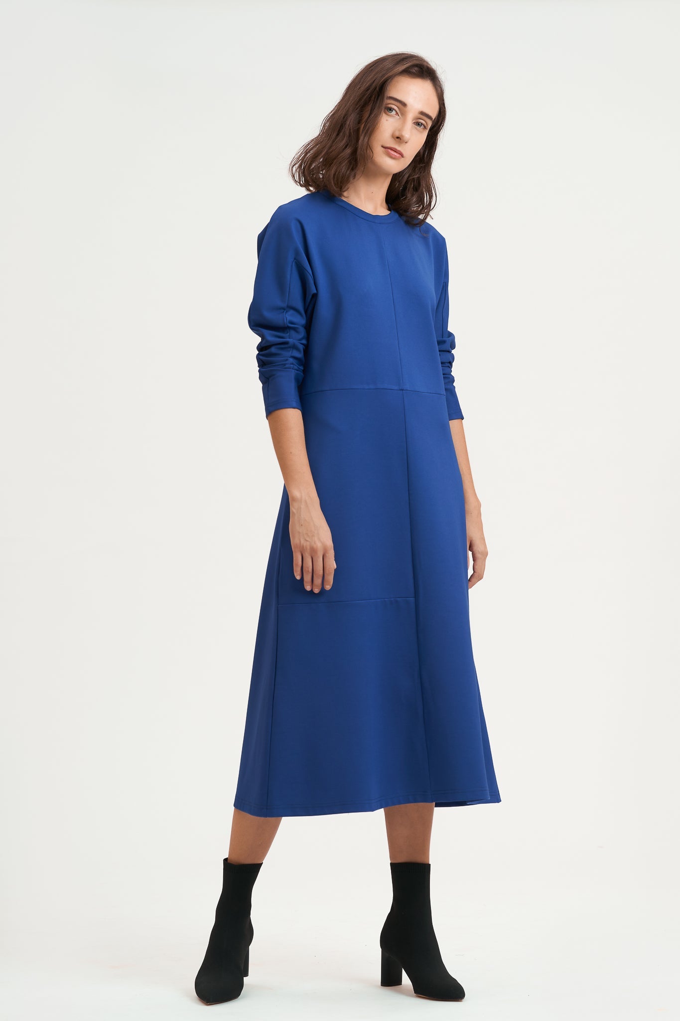 A woman with shoulder length hair is wearing an ankle length blue dress with long sleeves. She is also wearing black boots.