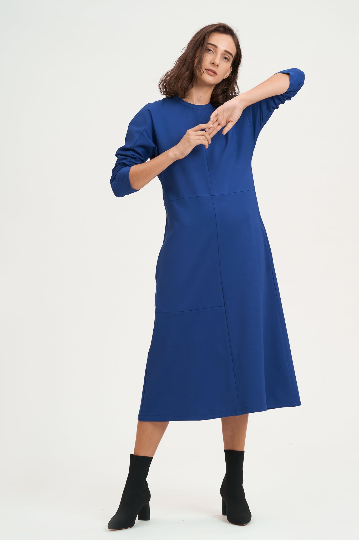 A woman with shoulder length hair is wearing an ankle length blue dress with long sleeves. She is also wearing black boots.