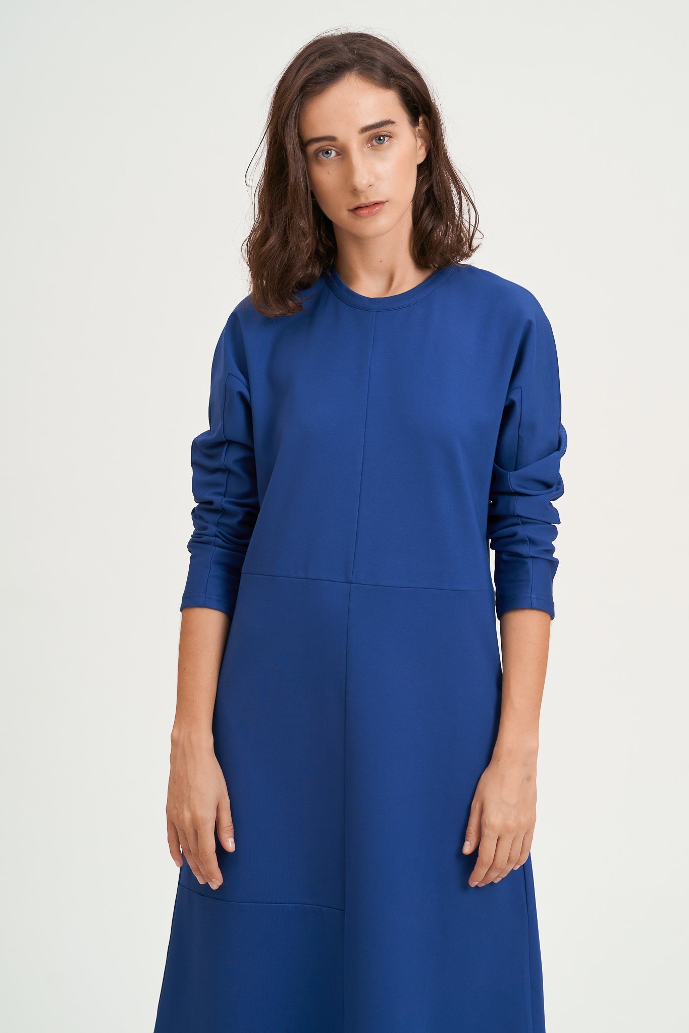 A woman with shoulder length hair is wearing an ankle length blue dress with long sleeves.