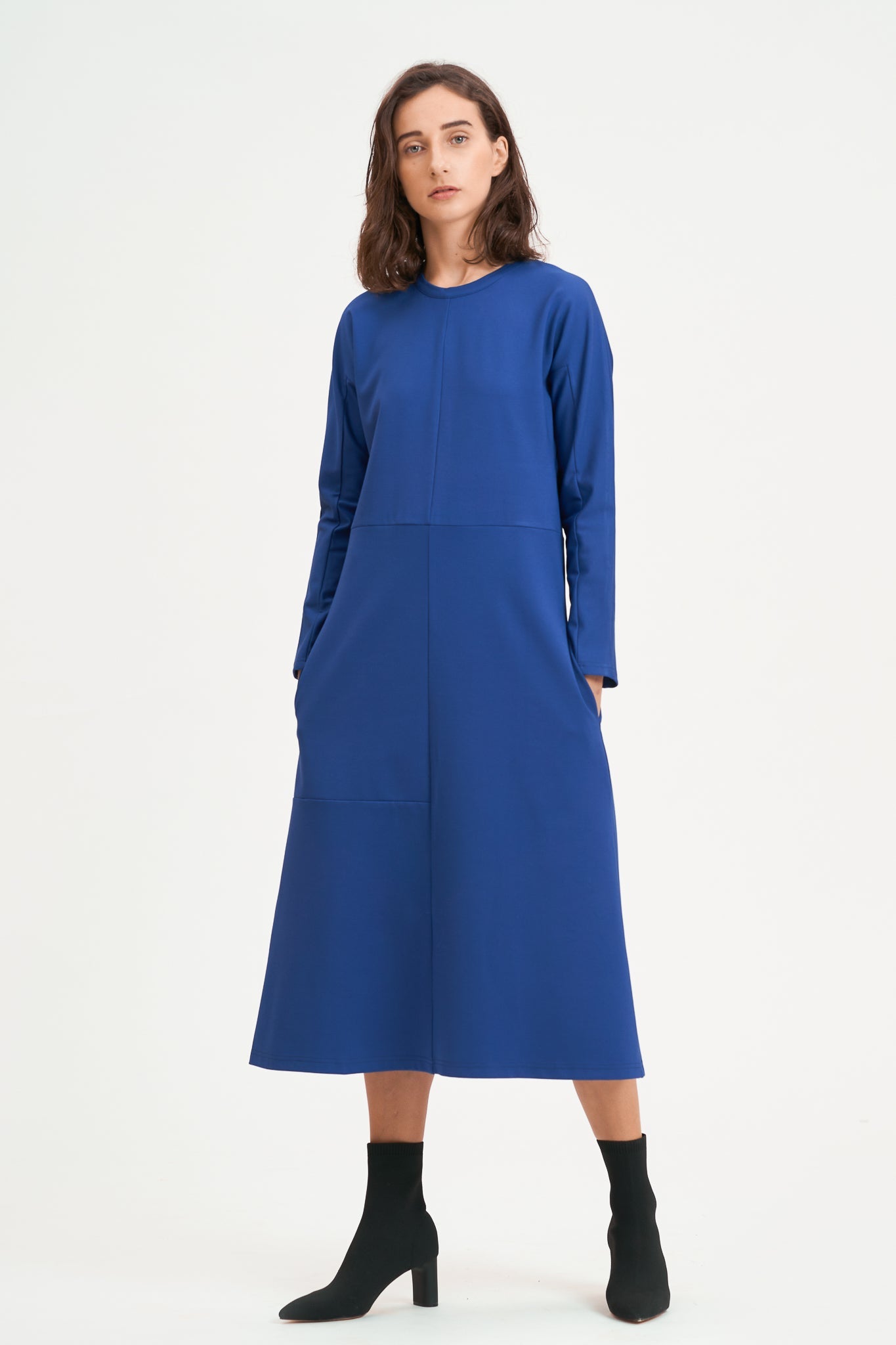 A woman with shoulder length hair is wearing an ankle length blue dress with long sleeves. She is also wearing black boots.