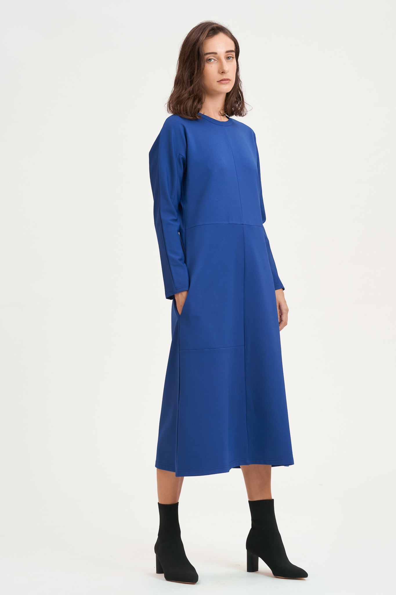 A woman with shoulder length hair is wearing an ankle length blue dress with long sleeves. She is also wearing black boots.