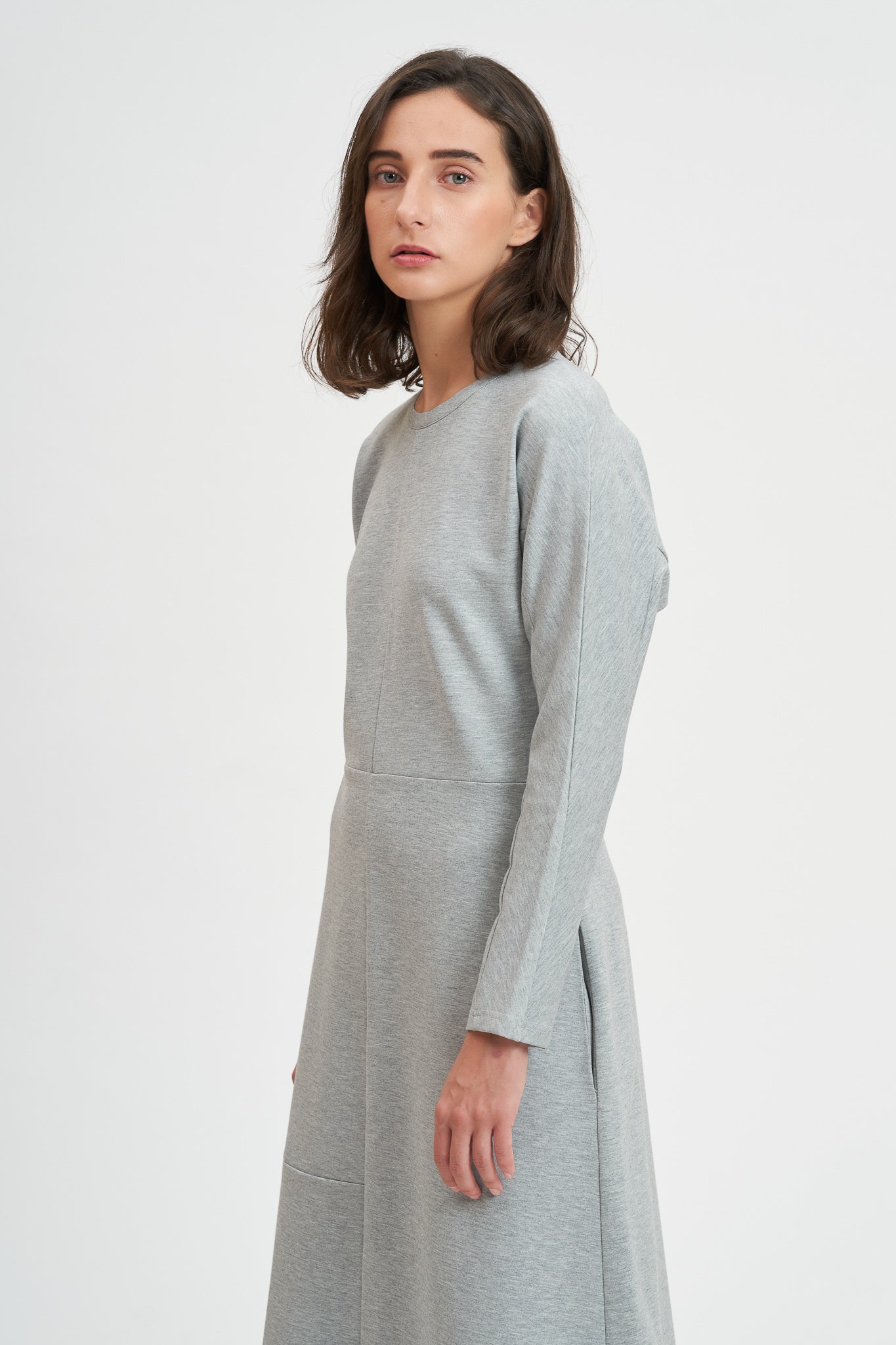 A woman with shoulder length hair is wearing an ankle length gray dress with long sleeves.