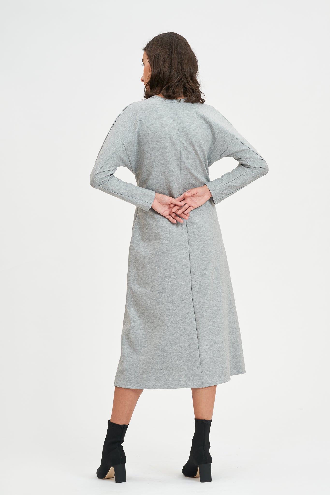 A woman with shoulder length hair is wearing an ankle length gray dress with long sleeves. She is also wearing black boots.