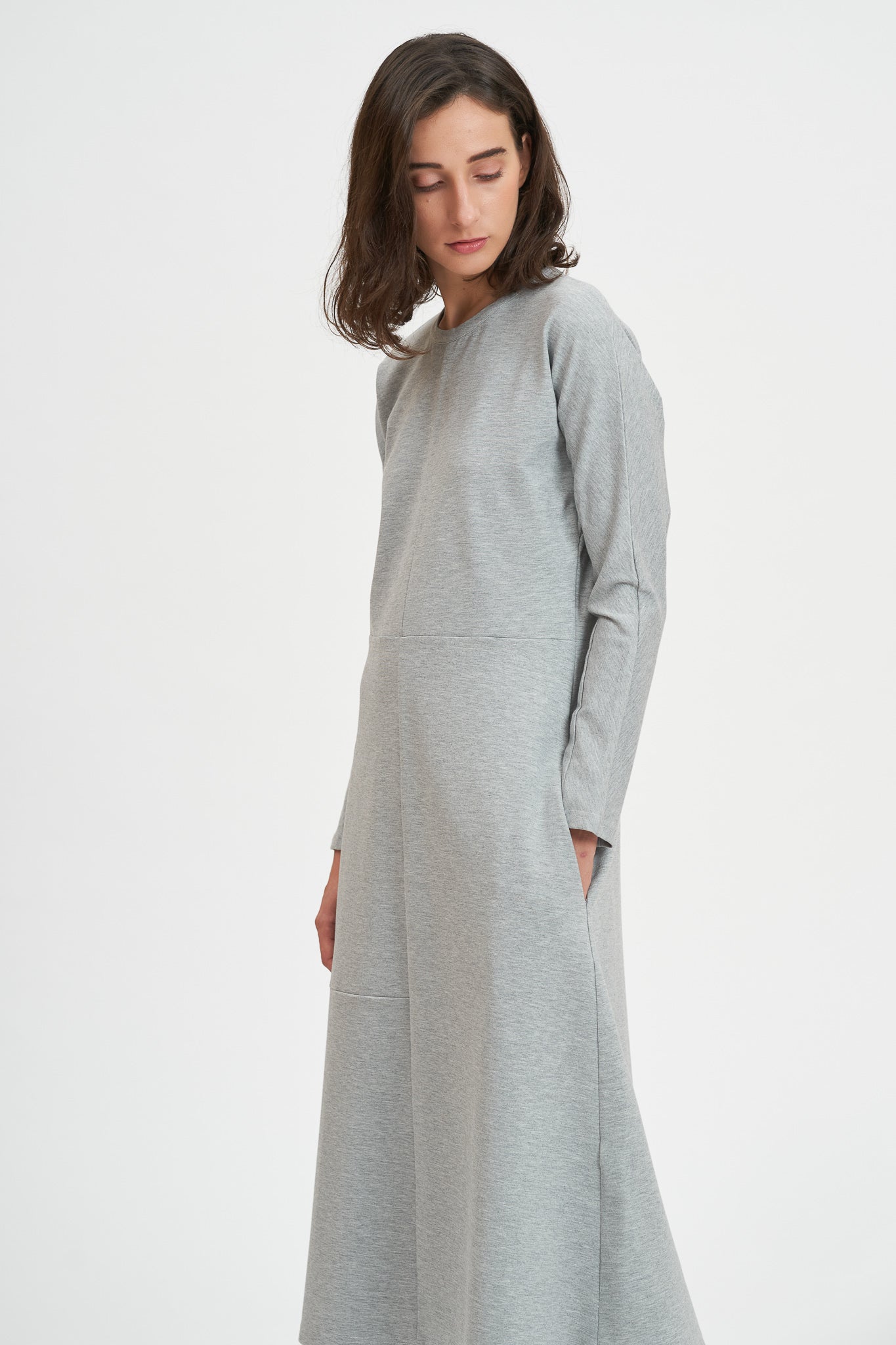 A woman with shoulder length hair is wearing an ankle length gray dress with long sleeves.