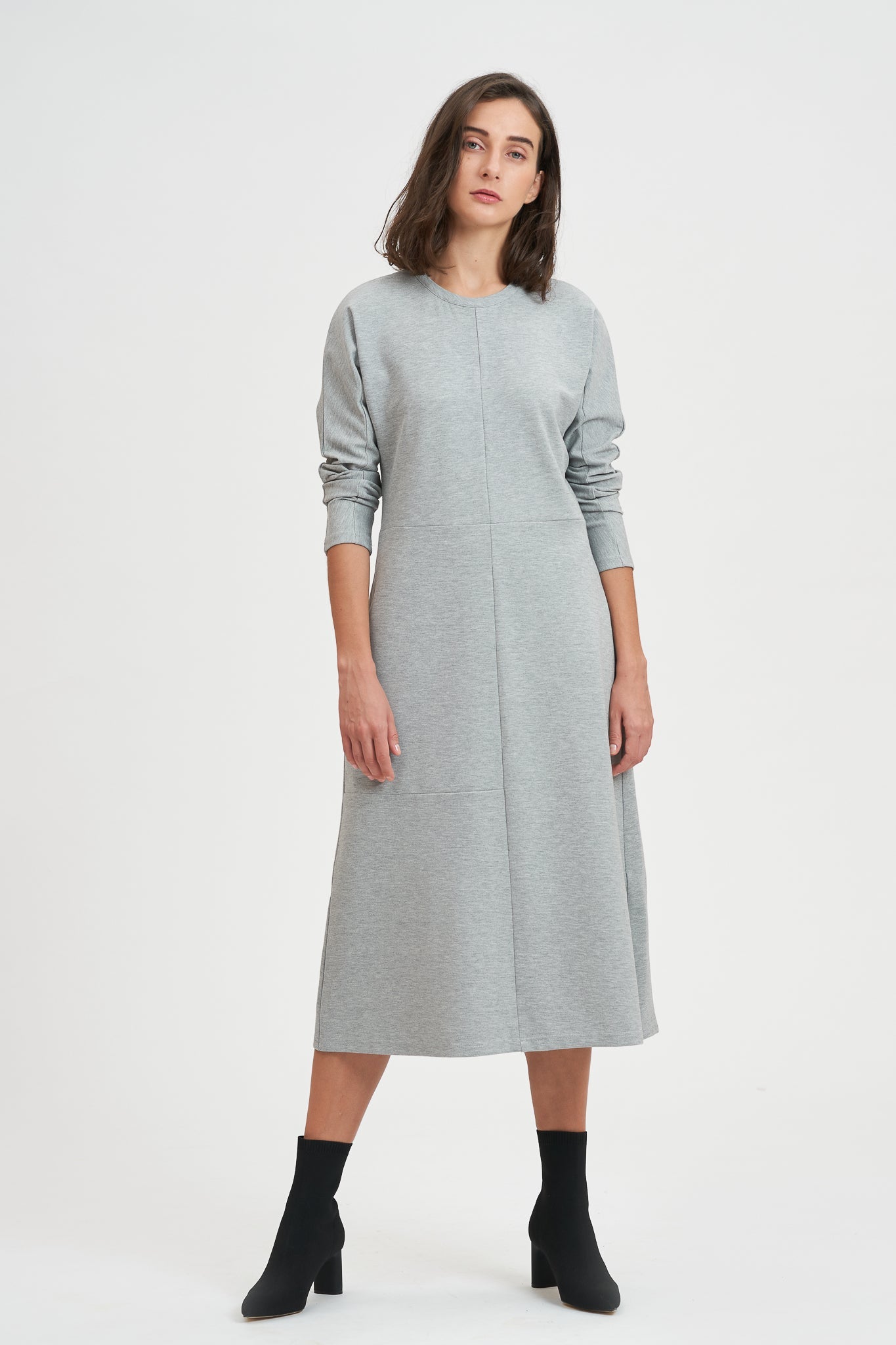 A woman with shoulder length hair is wearing an ankle length gray dress with long sleeves. She is also wearing black boots.