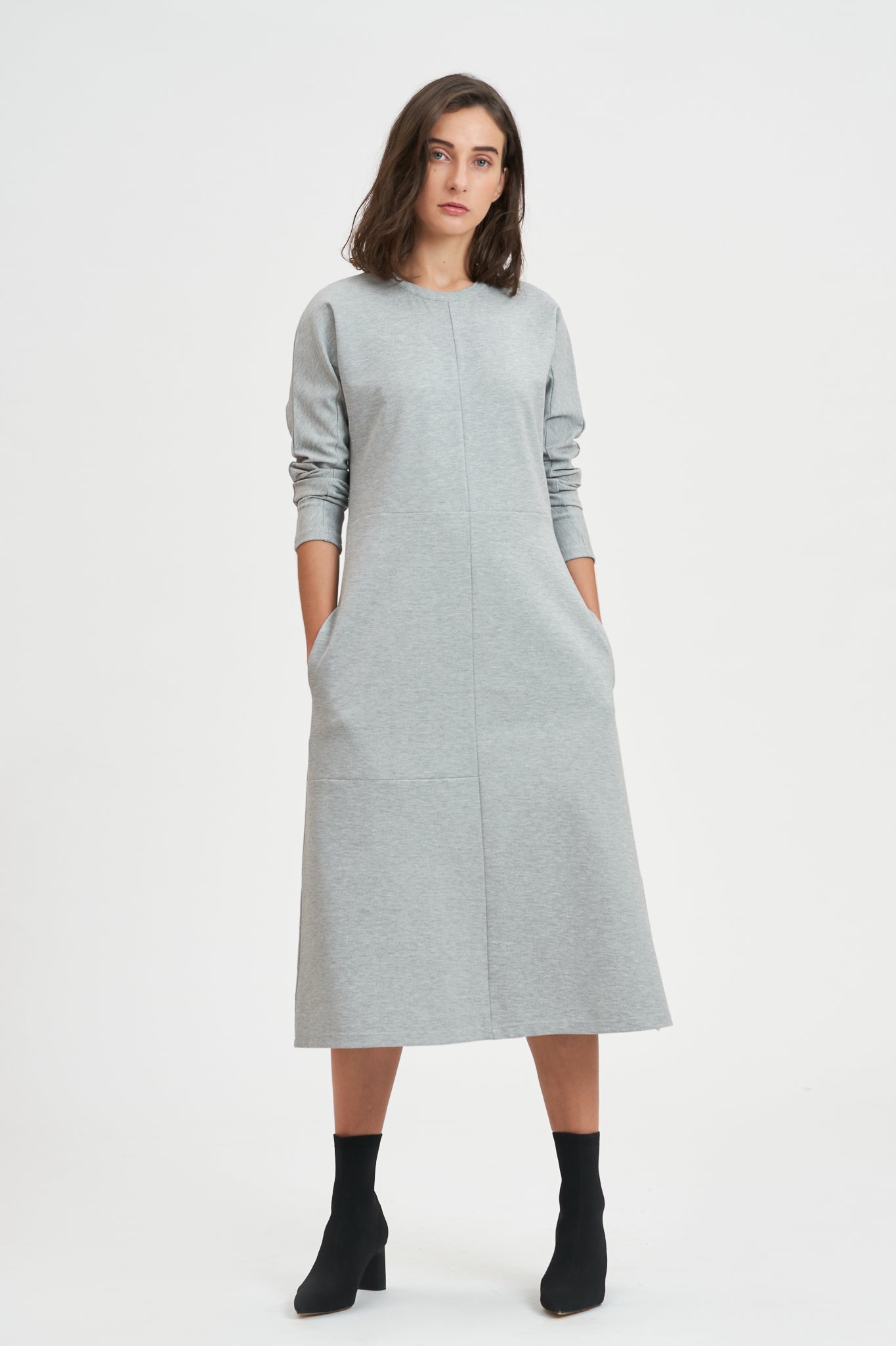 A woman with shoulder length hair is wearing an ankle length gray dress with long sleeves. She is also wearing black boots.