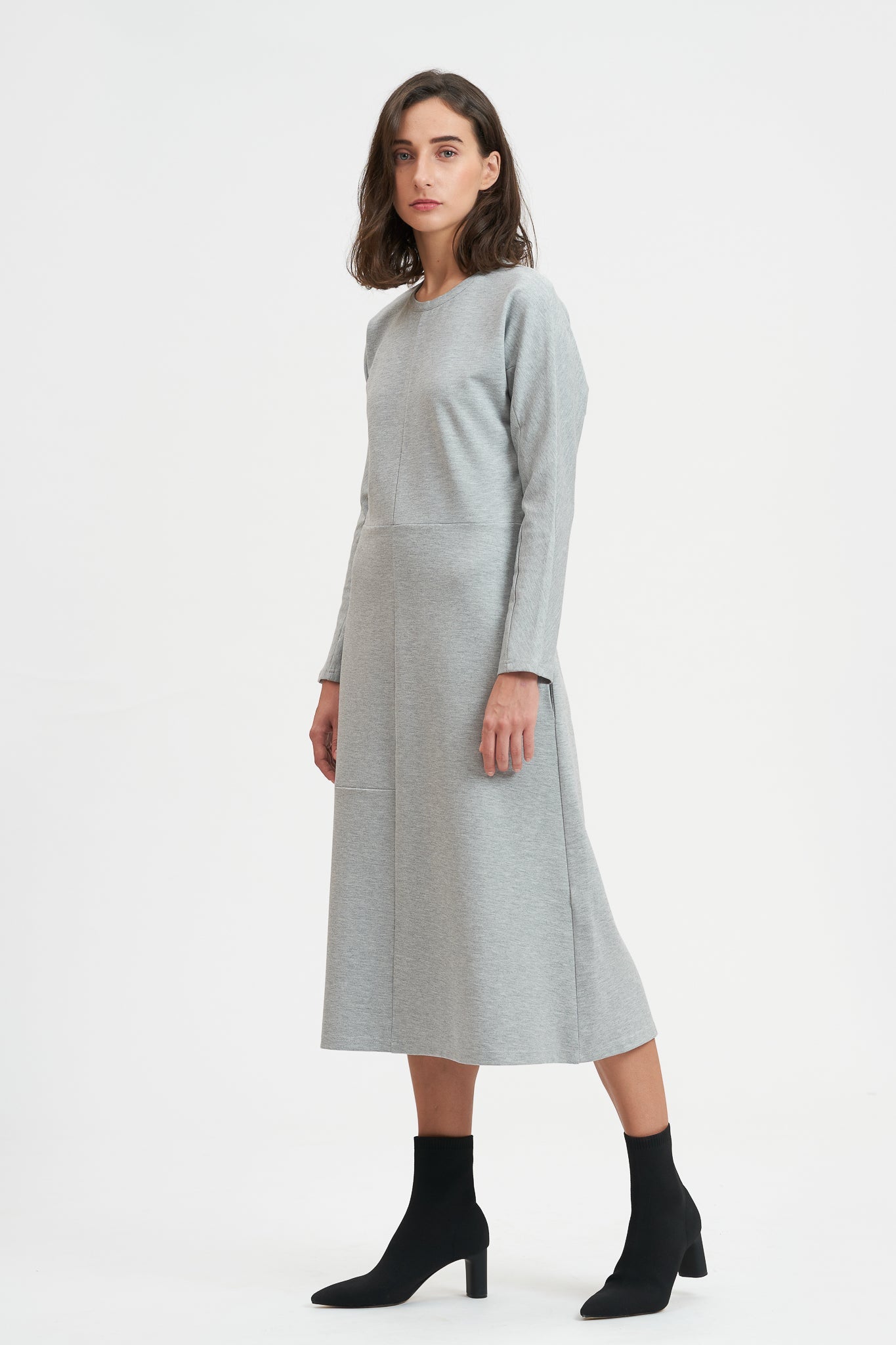A woman with shoulder length hair is wearing an ankle length gray dress with long sleeves. She is also wearing black boots.