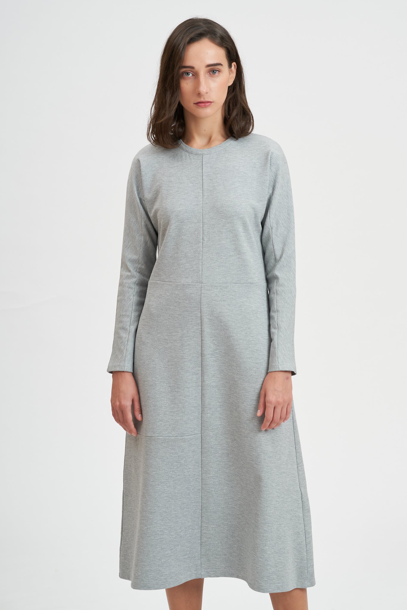 A woman with shoulder length hair is wearing an ankle length gray dress with long sleeves.
