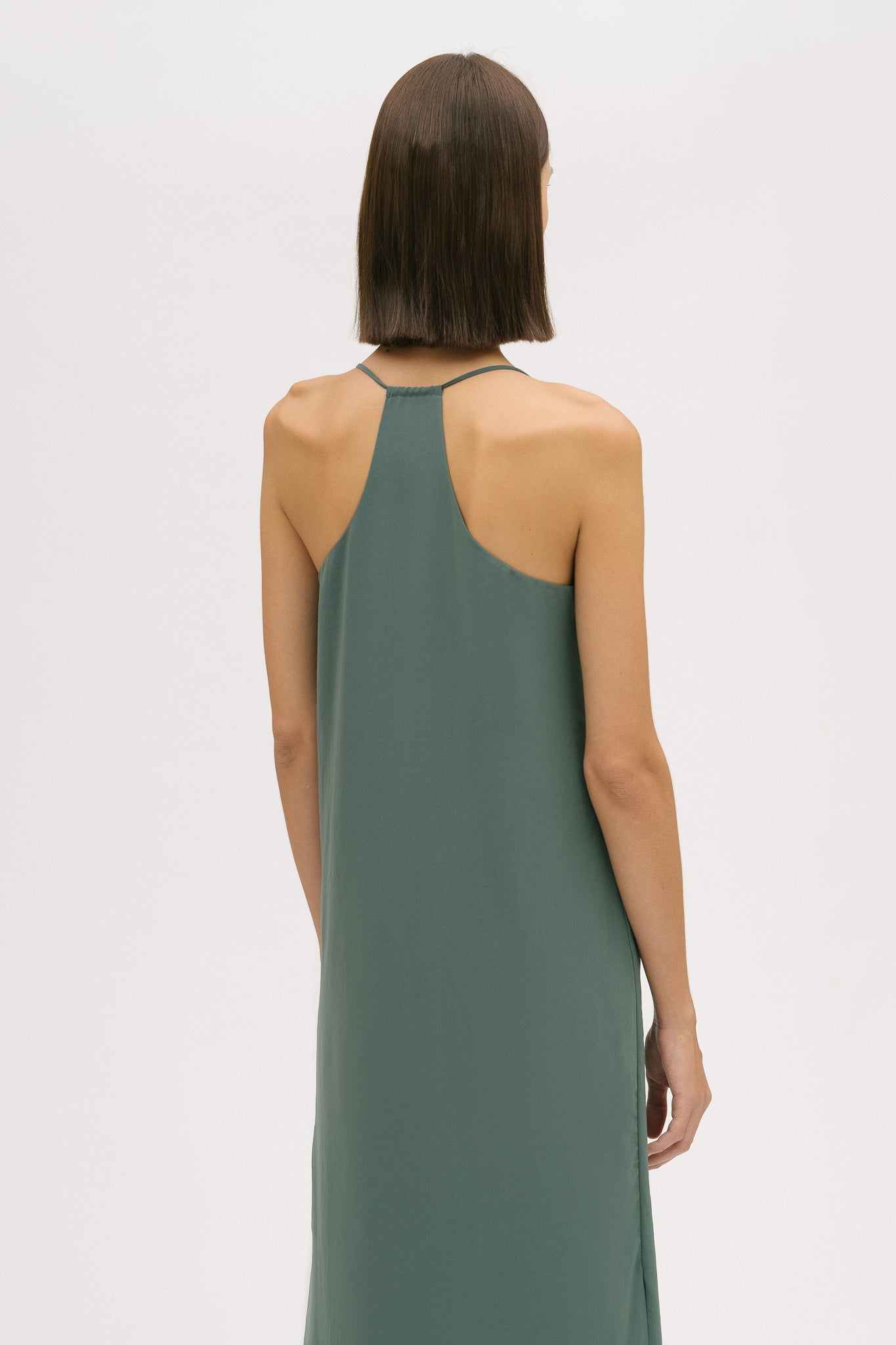 A woman with short brown hair is wearing a long green silky dress with straps.