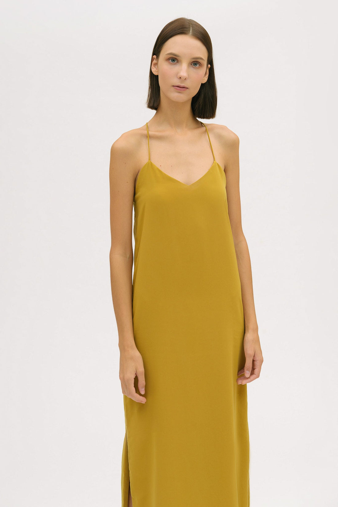 A woman with short brown hair is wearing a long yellow silky dress with straps. She has beige mules on.  Edit alt text