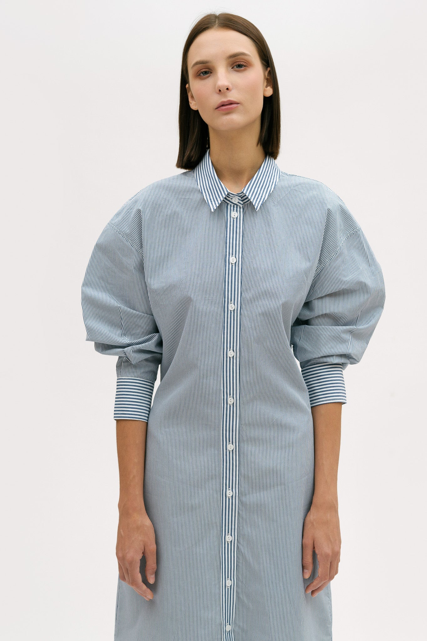 A woman with short brown hair is wearing a knee length blue and white pin striped shirt dress.