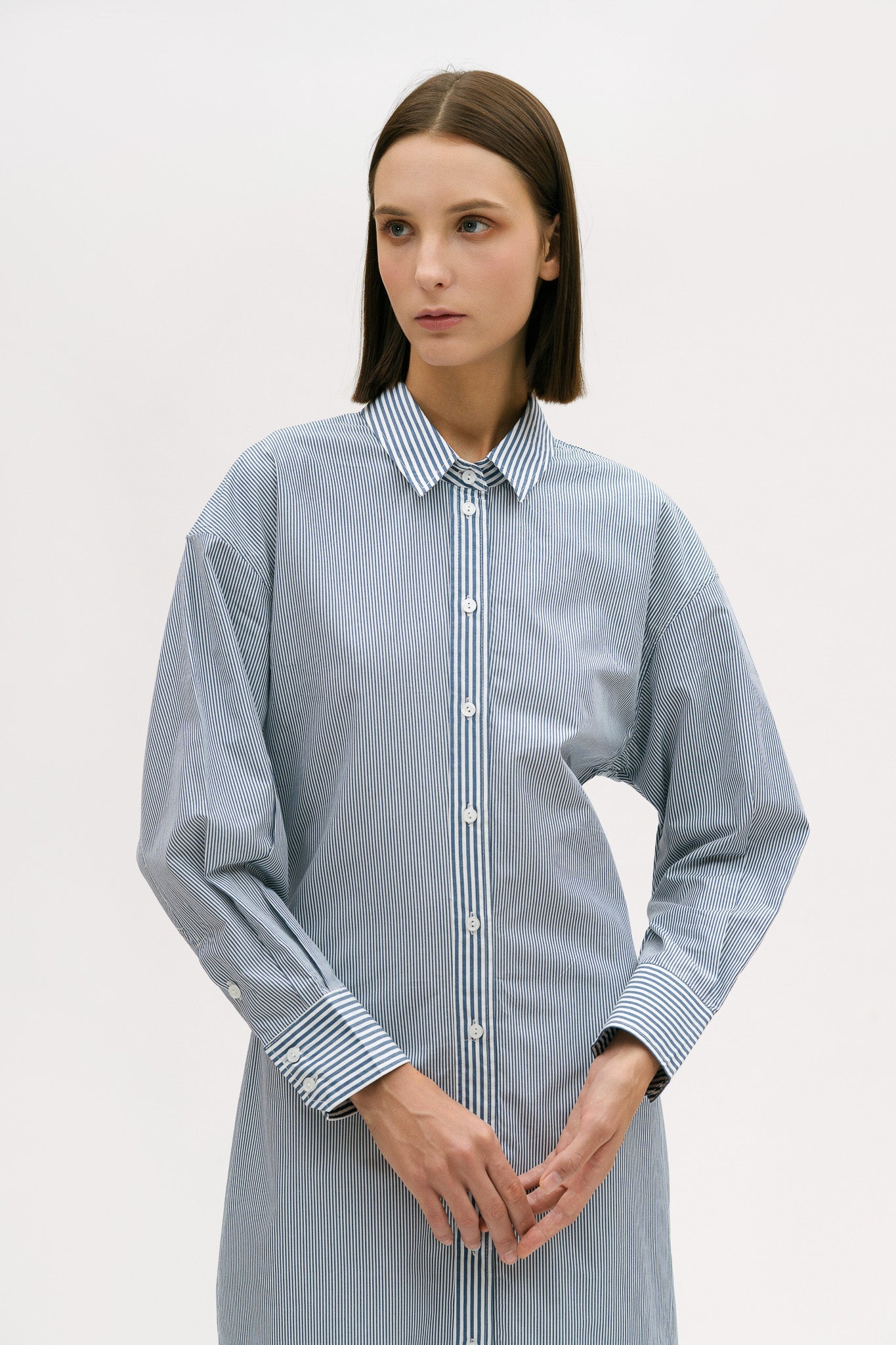 A woman with short brown hair is wearing a knee length blue and white pin striped shirt dress.