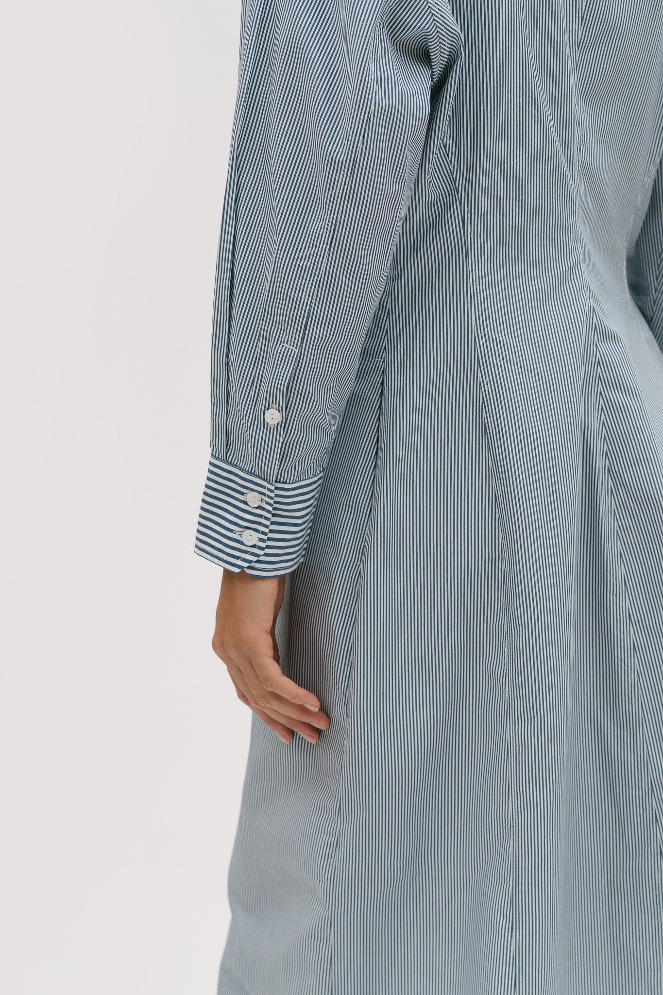 A woman with short brown hair is wearing a knee length blue and white pin striped shirt dress.