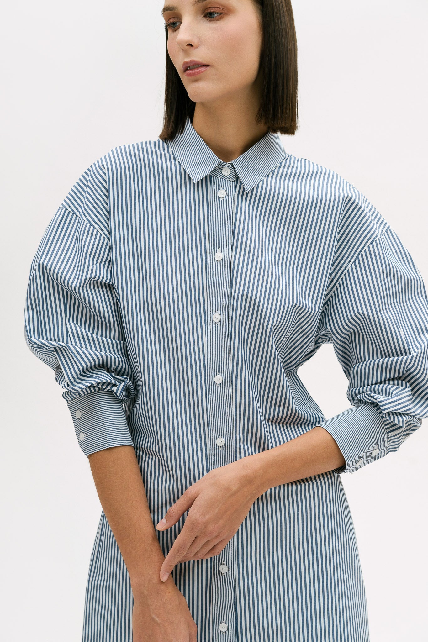 A woman with short brown hair is wearing a knee length blue and white pin striped shirt dress.