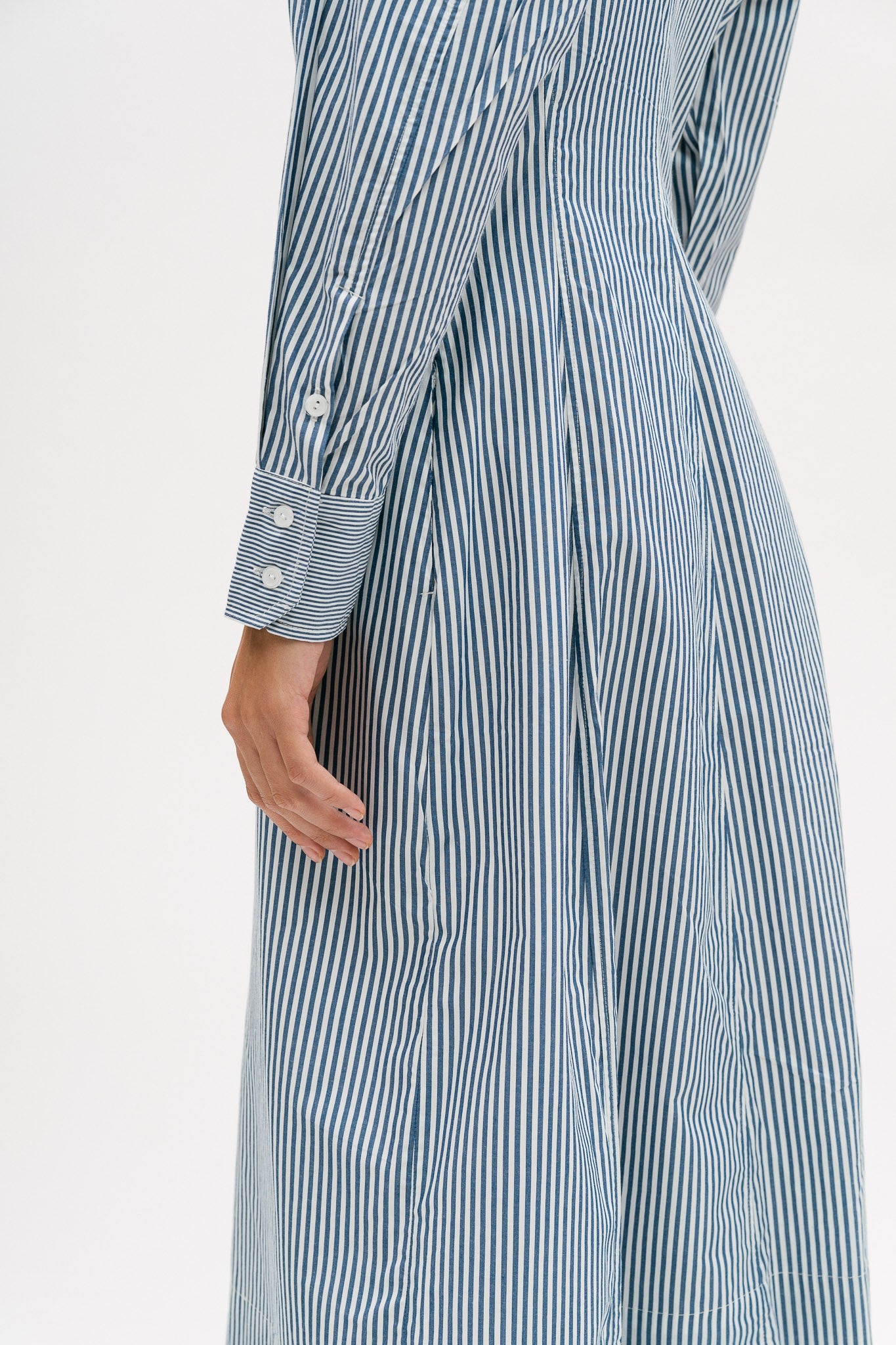A woman with short brown hair is wearing a knee length blue and white pin striped shirt dress.