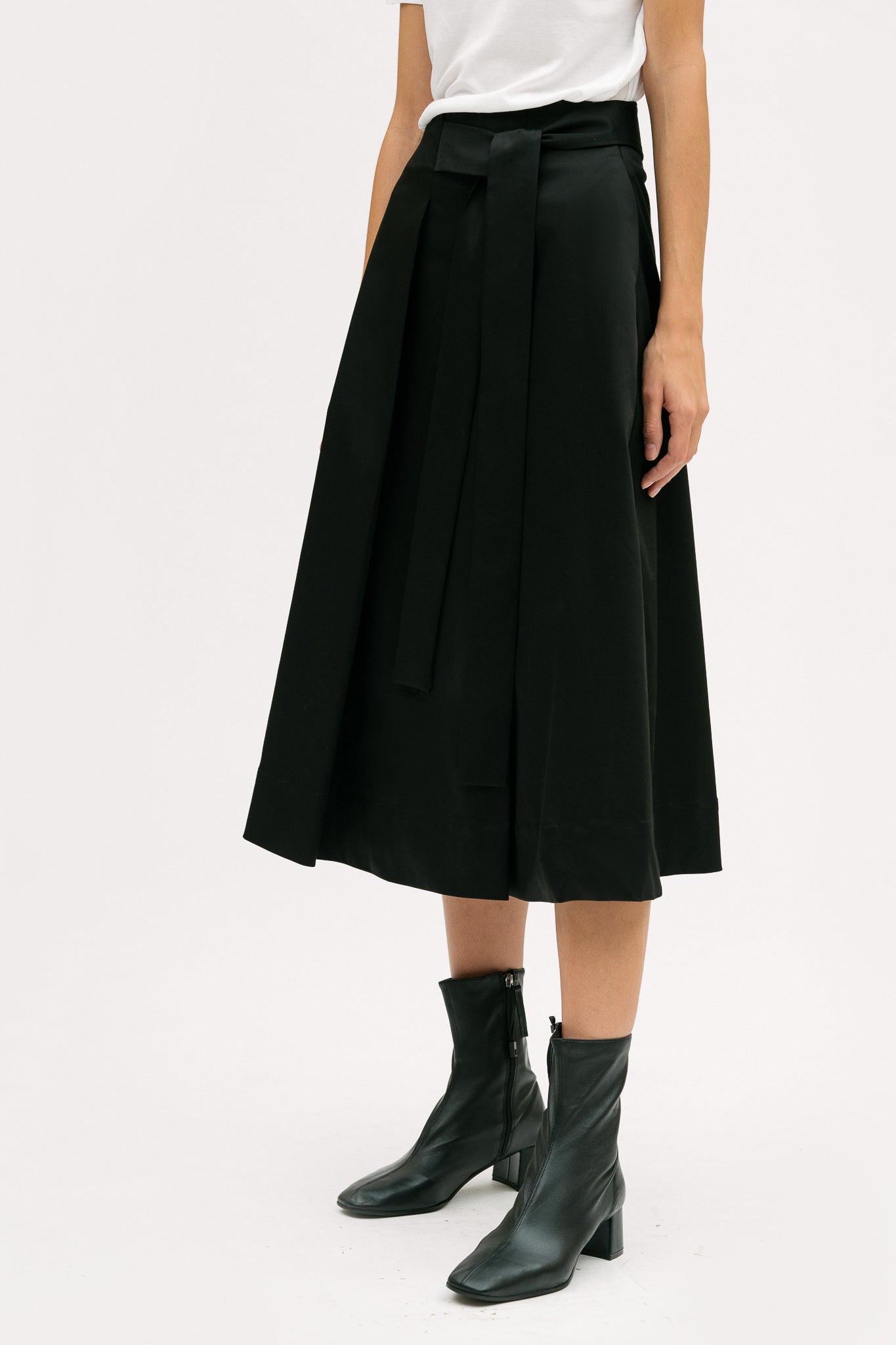 A woman is wearing a white t shirt and black calf length skirt. She is also wearing black boots