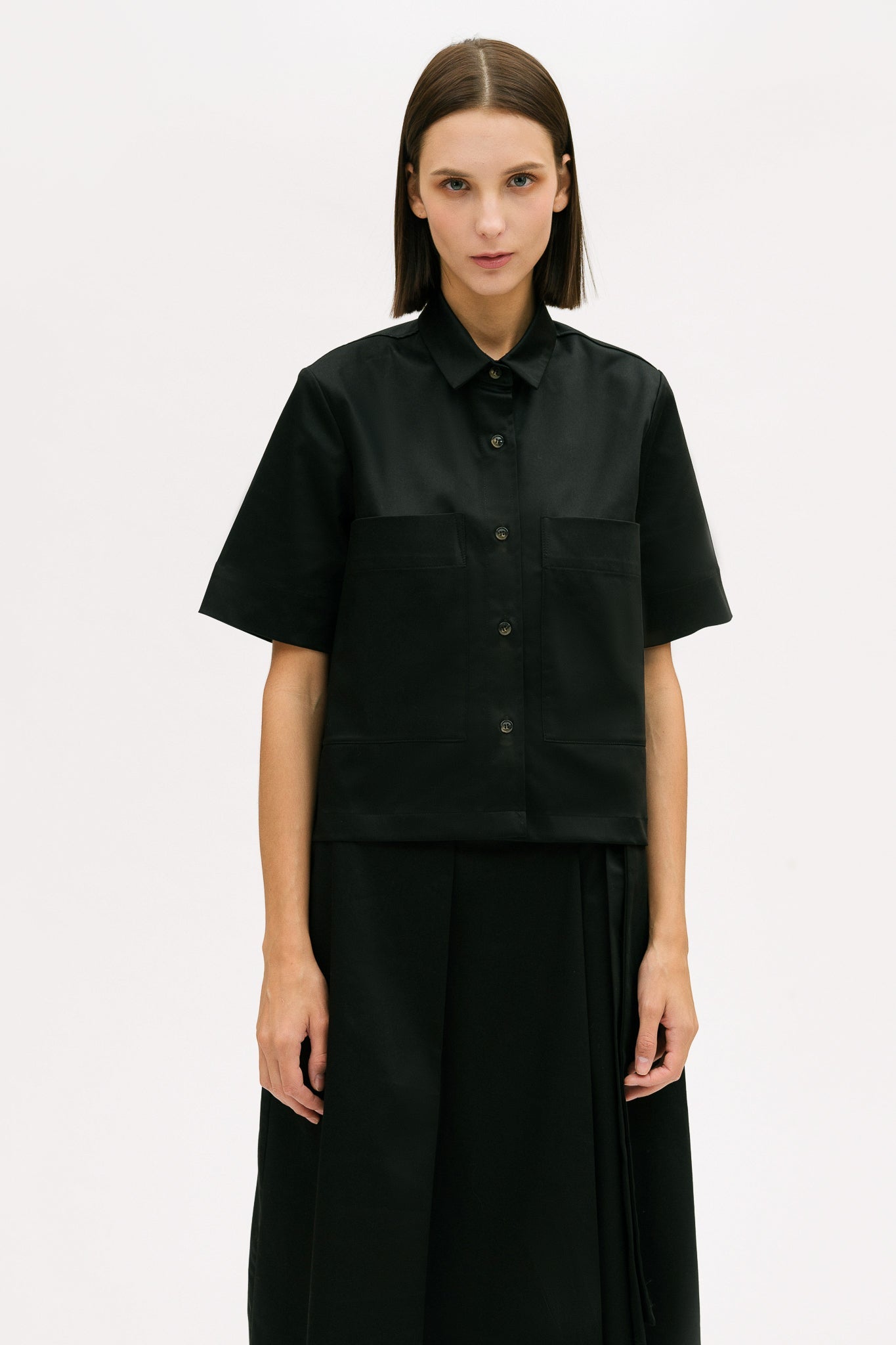 A woman with shoulder length brown hair is wearing a black utility shirt