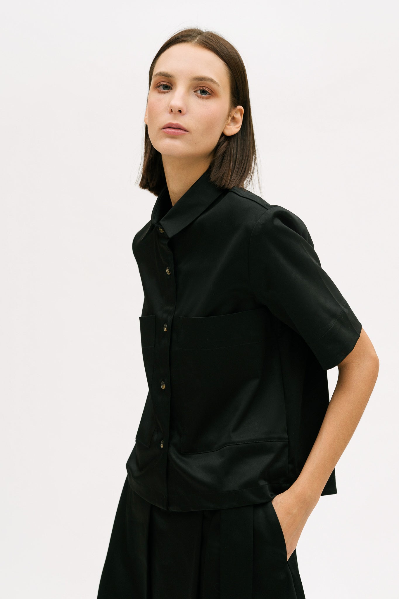 A woman with shoulder length brown hair is wearing a black utility shirt