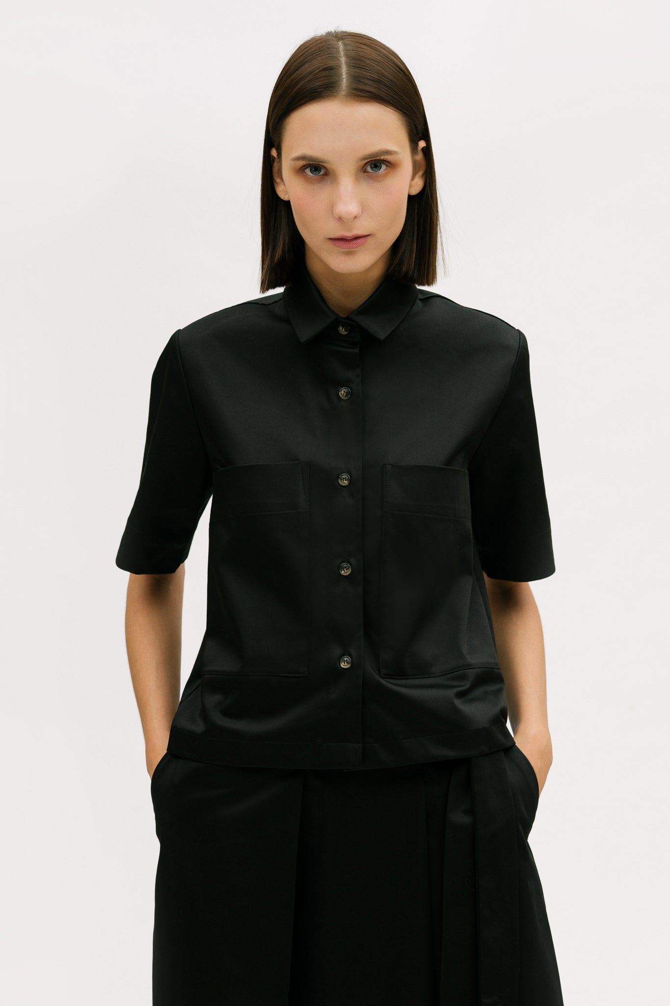 A woman with shoulder length brown hair is wearing a black utility shirt