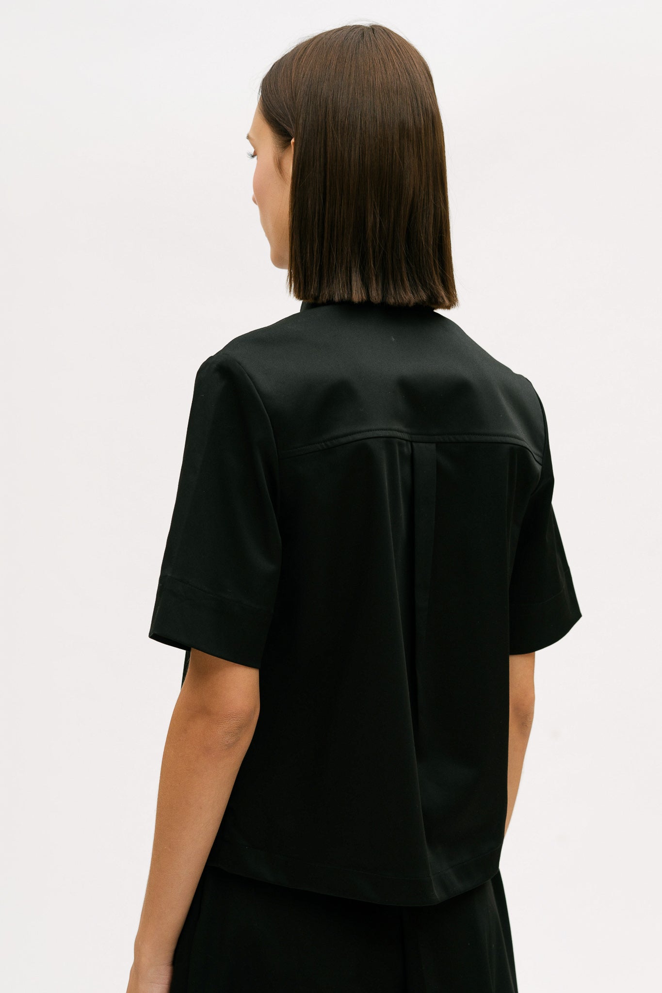 A woman with shoulder length brown hair is wearing a black utility shirt