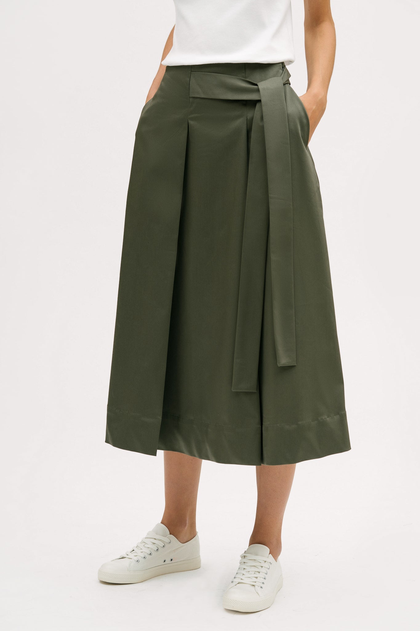A woman is wearing a white t shirt and green calf length skirt. She is also wearing white tennis shoes.