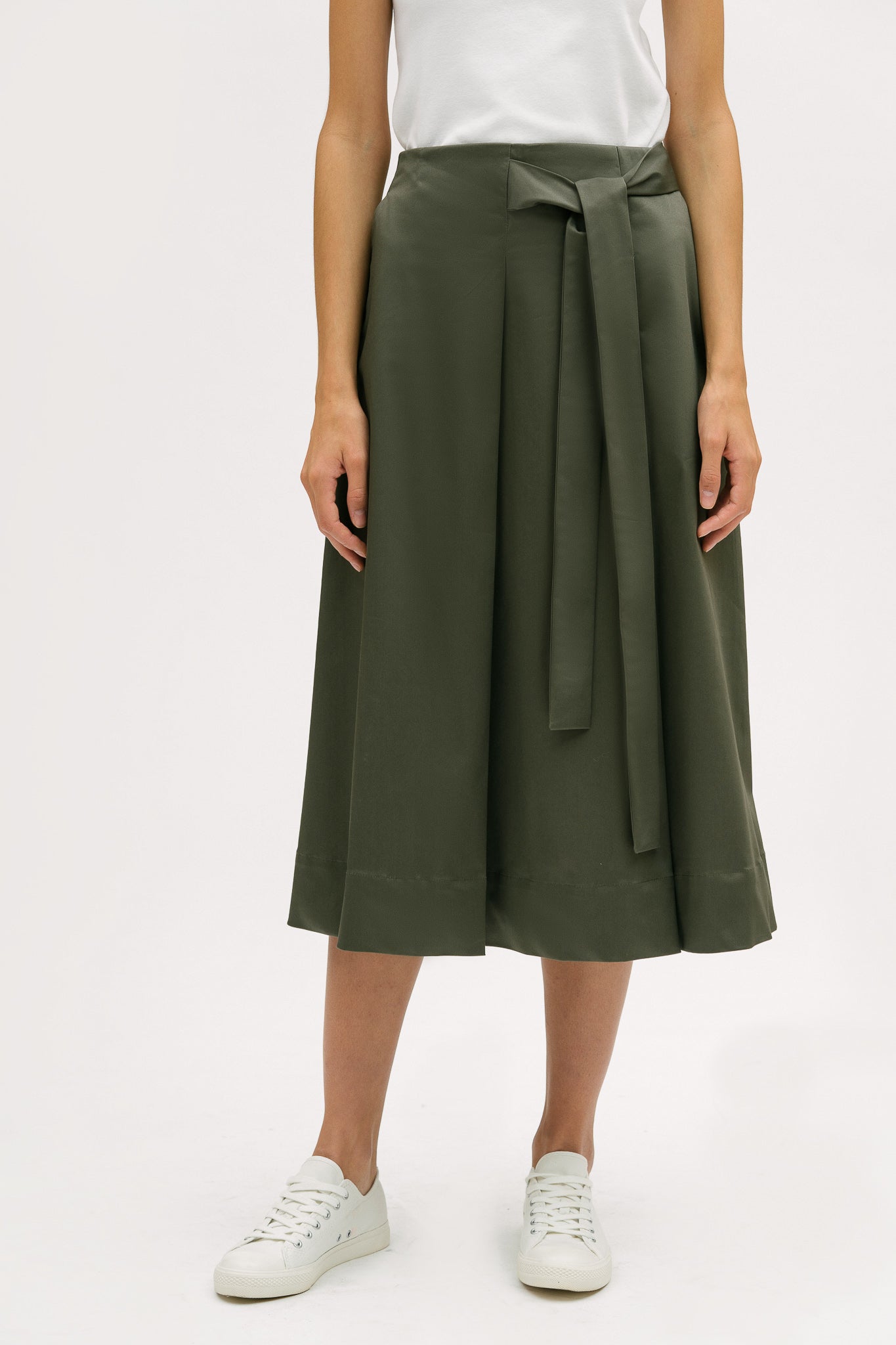 A woman is wearing a white t shirt and green calf length skirt. She is also wearing white tennis shoes.