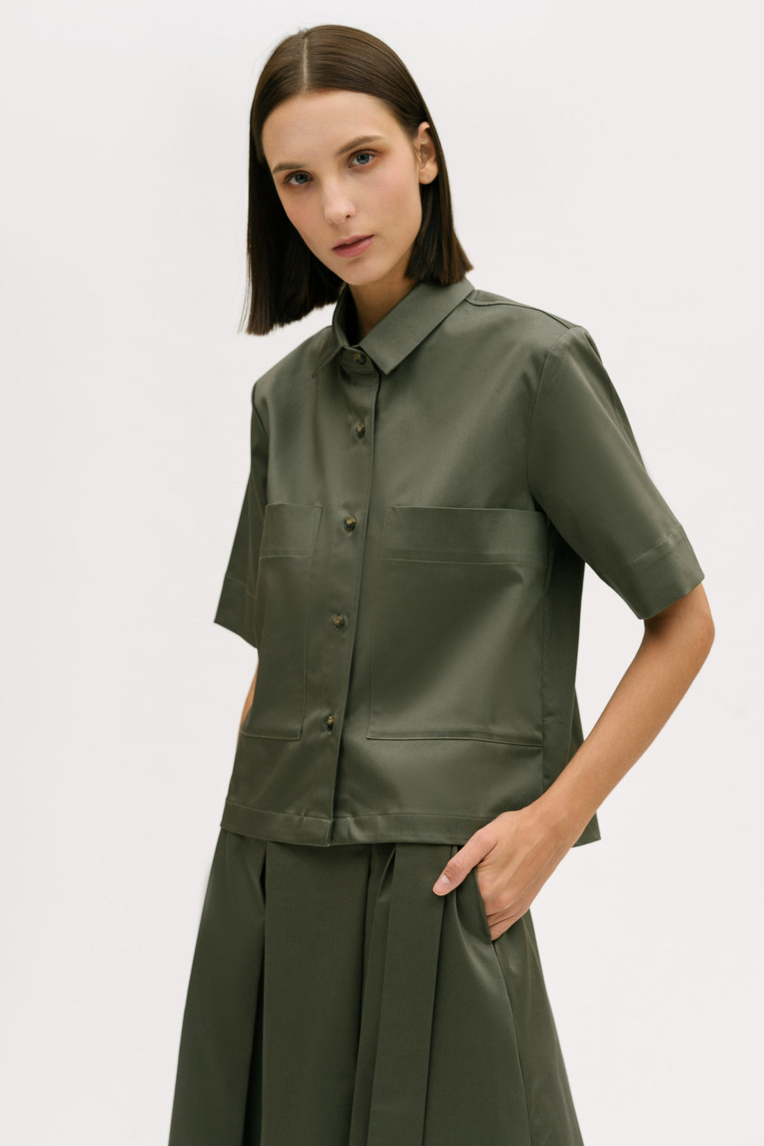 A woman with shoulder length brown hair is wearing a green utility shirt