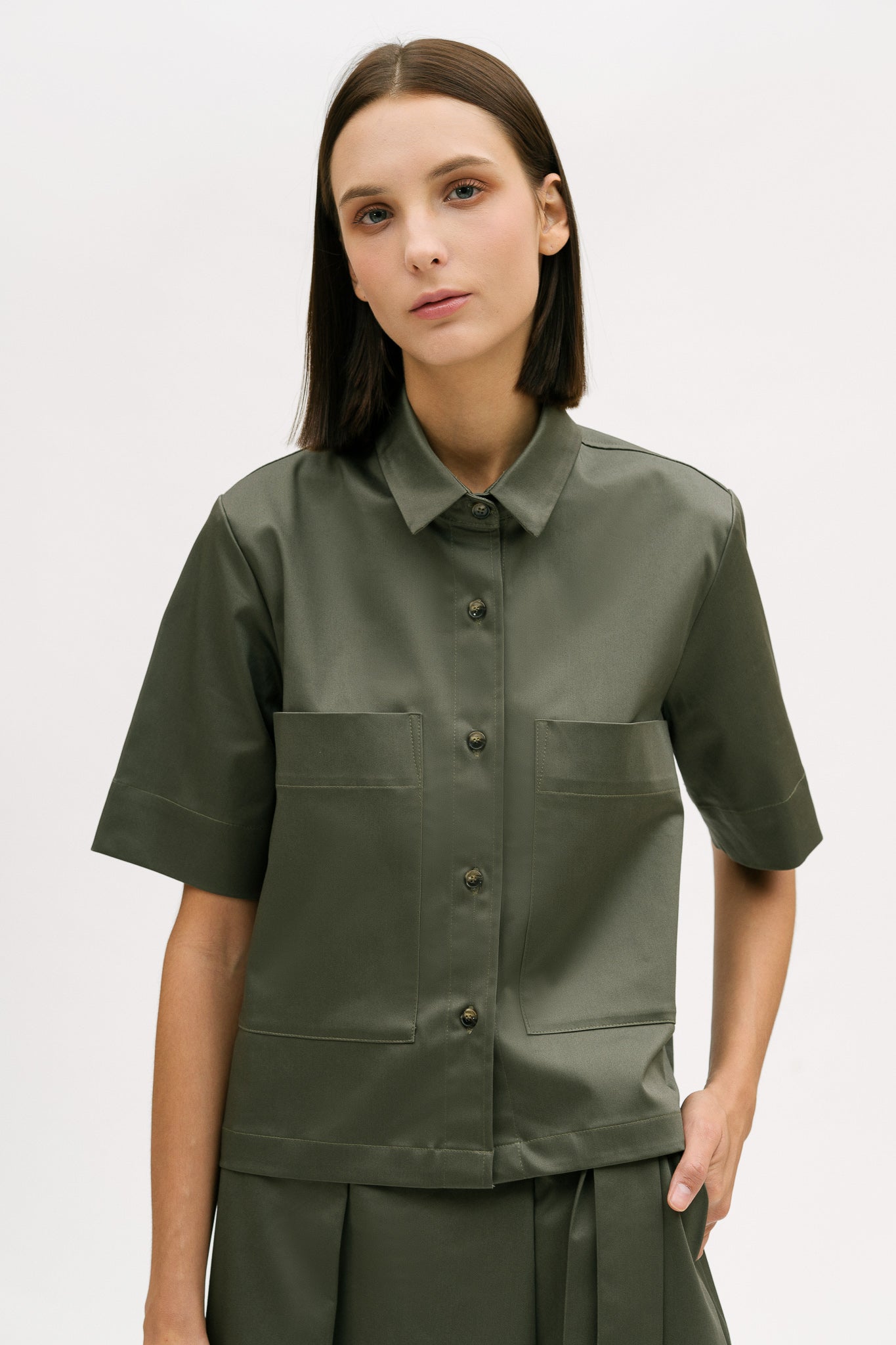 A woman with shoulder length brown hair is wearing a green utility shirt