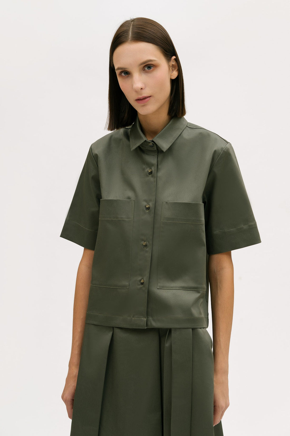 A woman with shoulder length brown hair is wearing a green utility shirt