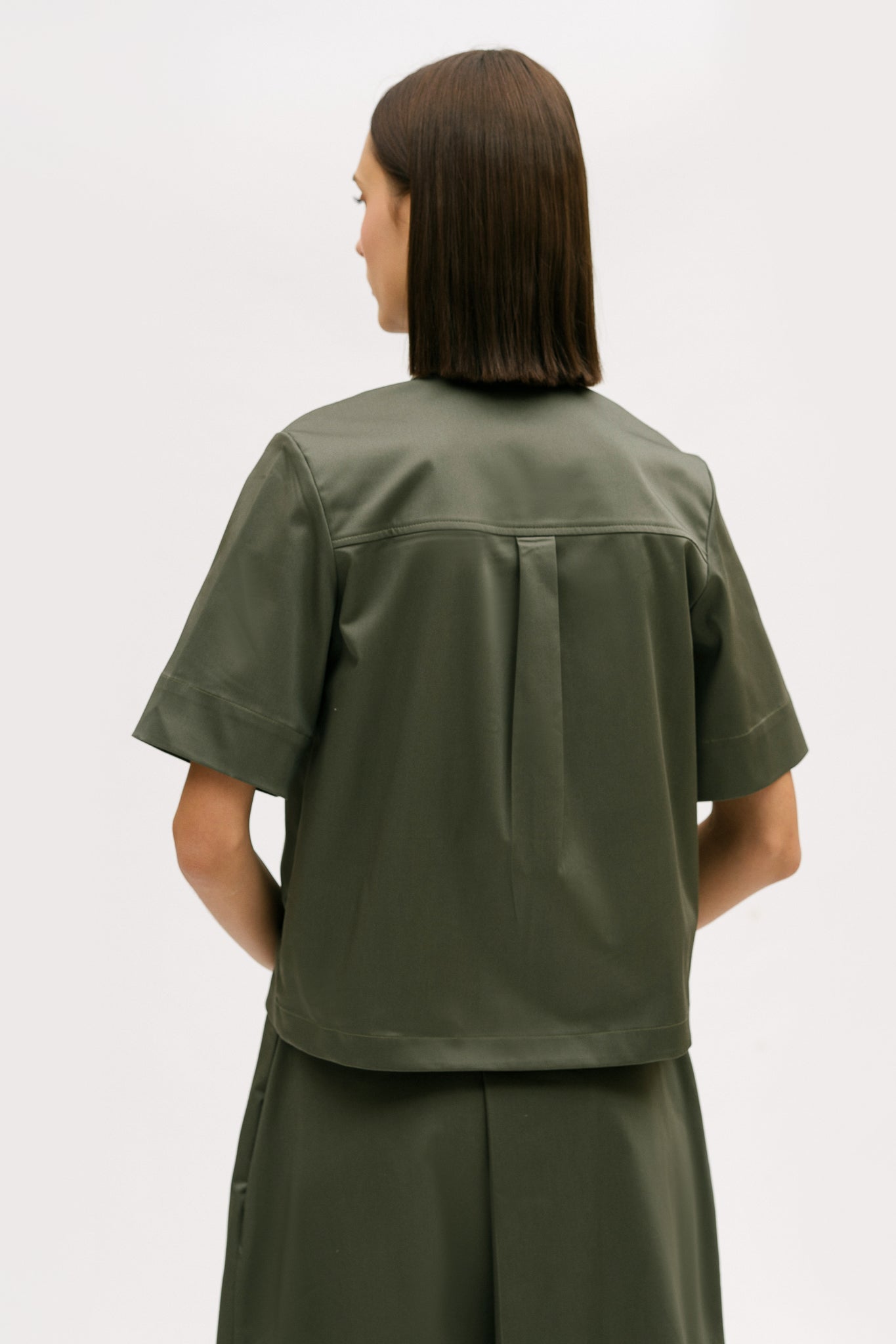 A woman with shoulder length brown hair is wearing a green utility shirt