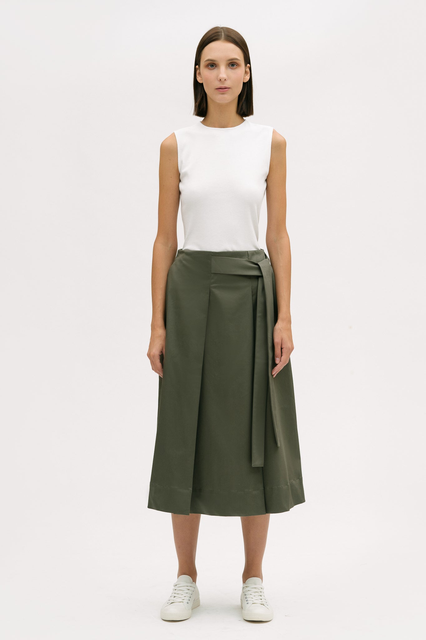 A woman is wearing a white t shirt and green calf length skirt. She is also wearing white tennis shoes.