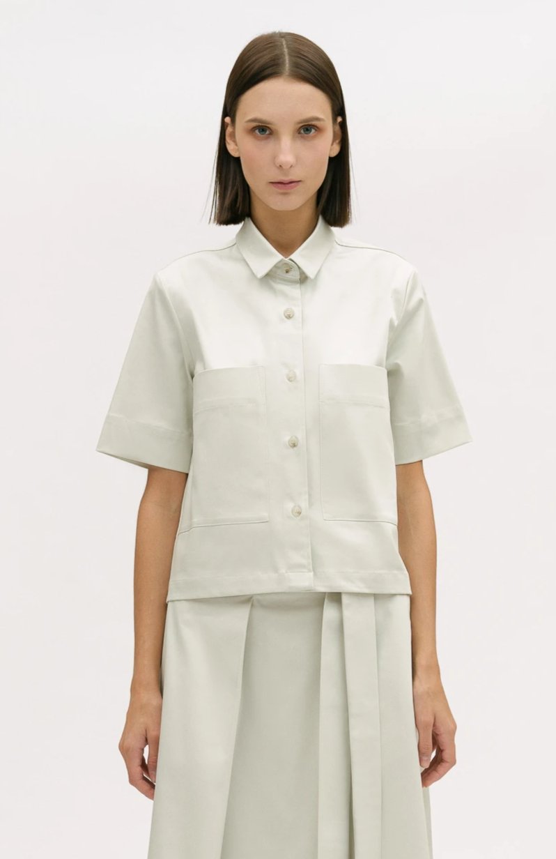 A woman with shoulder length brown hair is wearing an off-white utility shirt