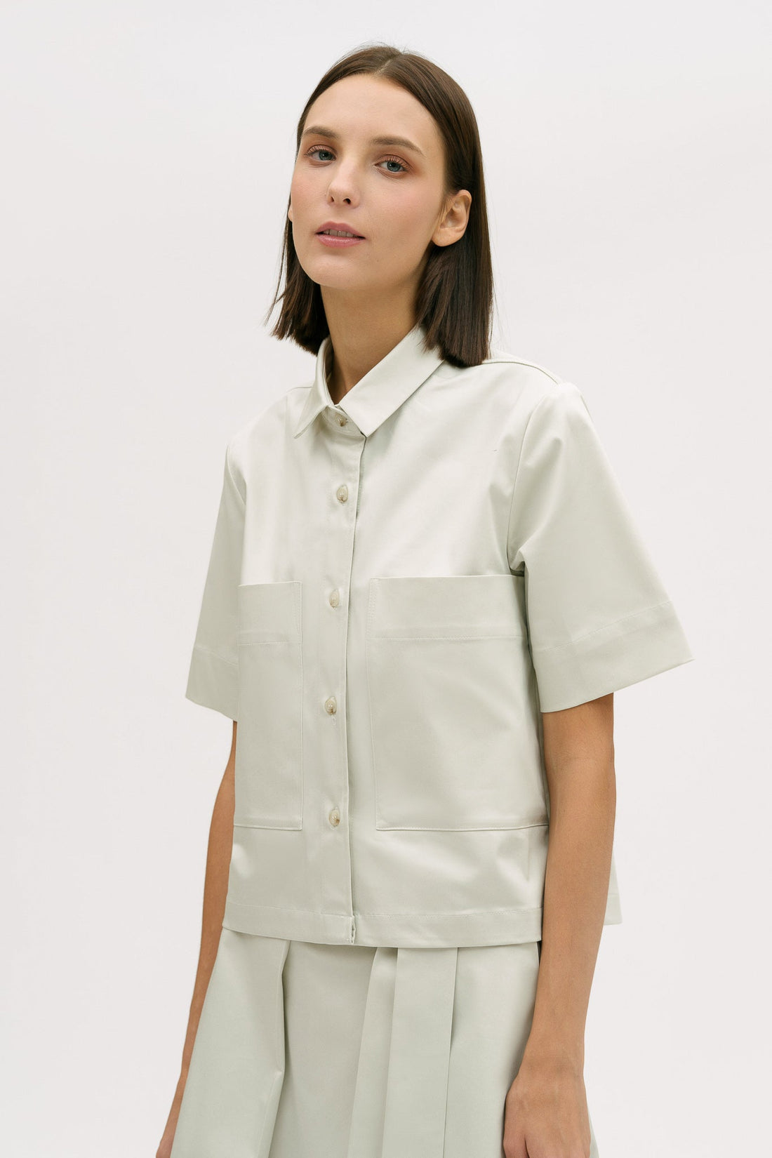 A woman with shoulder length brown hair is wearing an off-white utility shirt