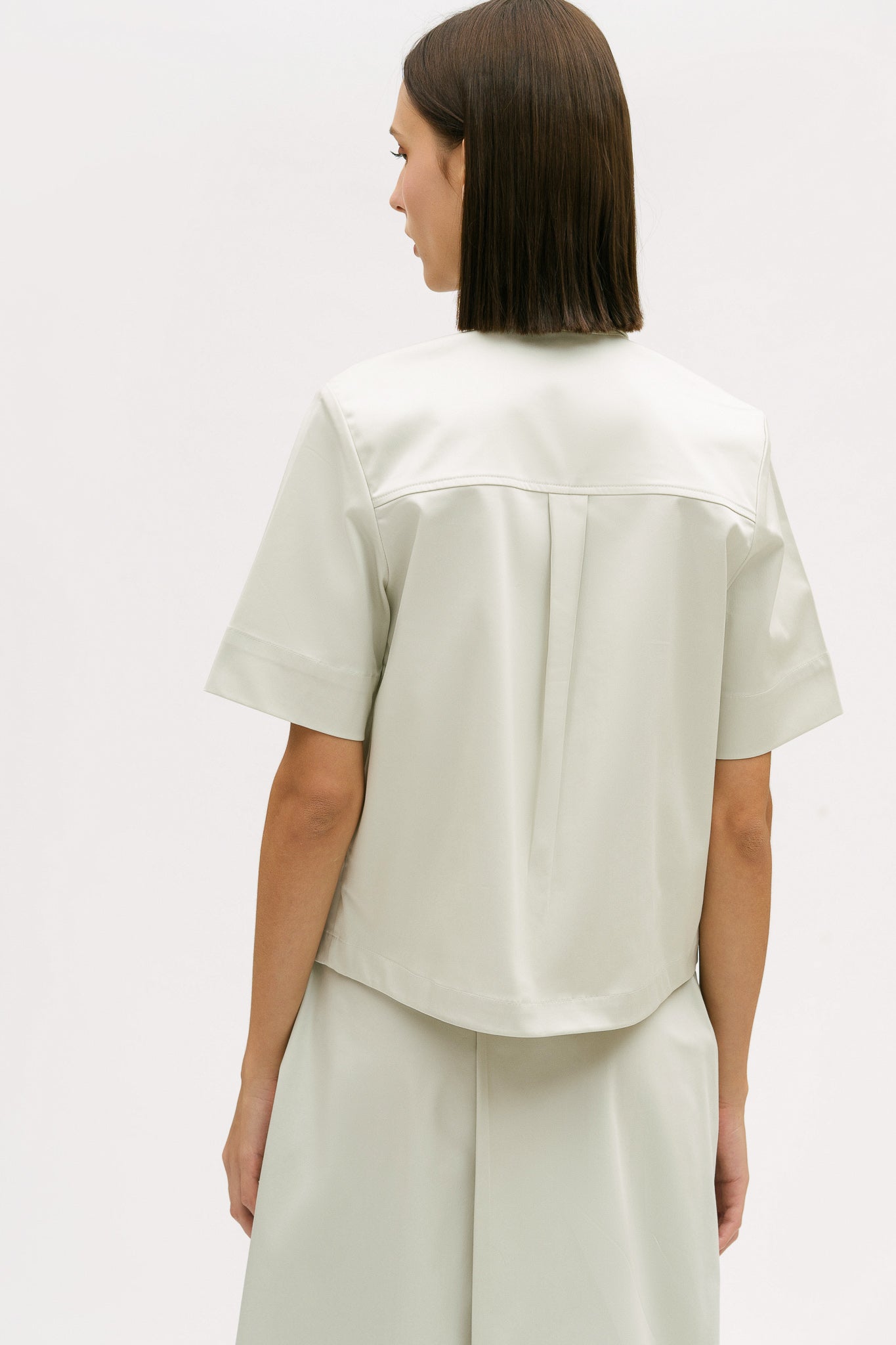 A woman with shoulder length brown hair is wearing an off-white utility shirt